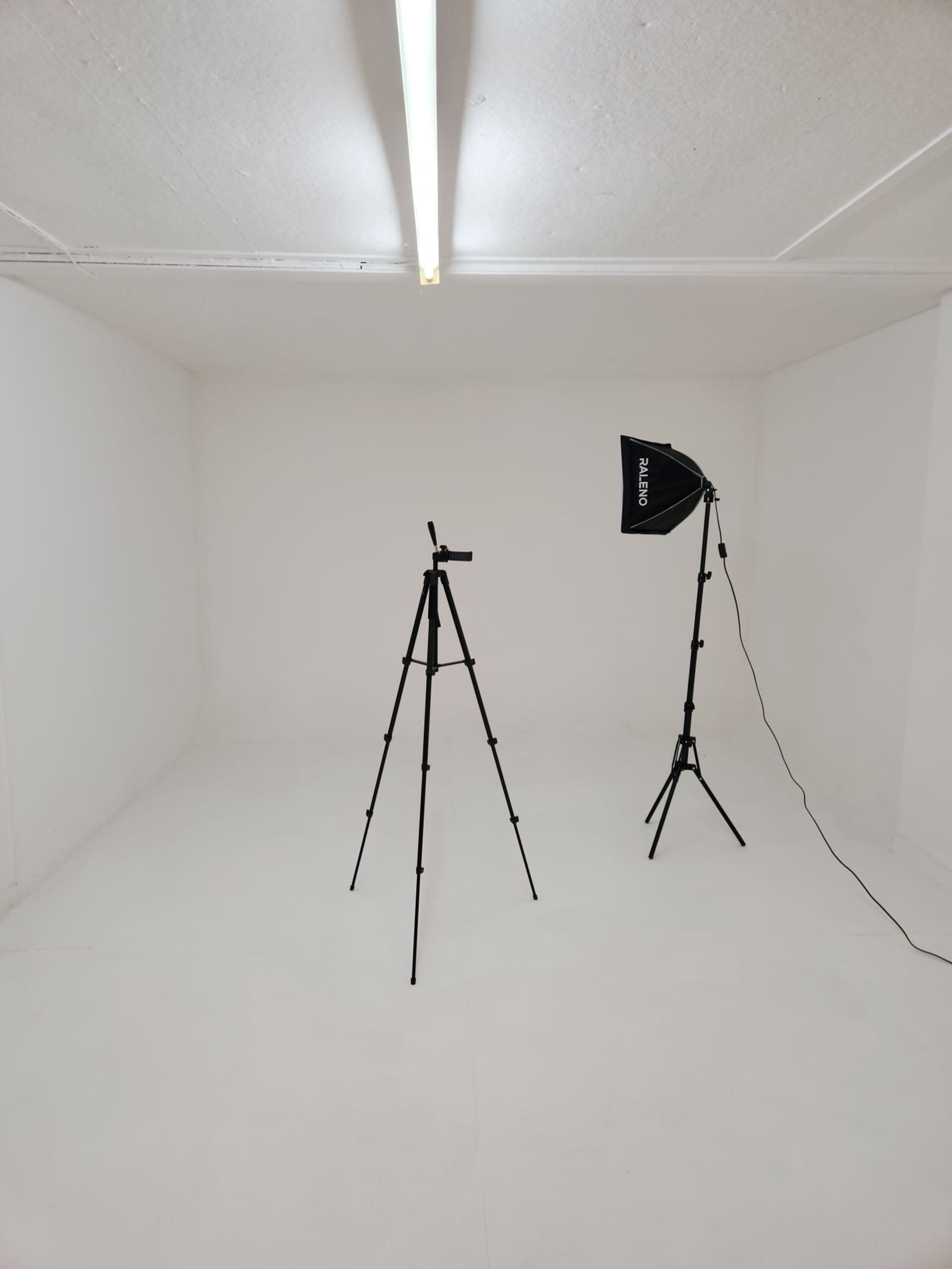 A sparse, white room features a tripod and a light stand positioned opposite each other.