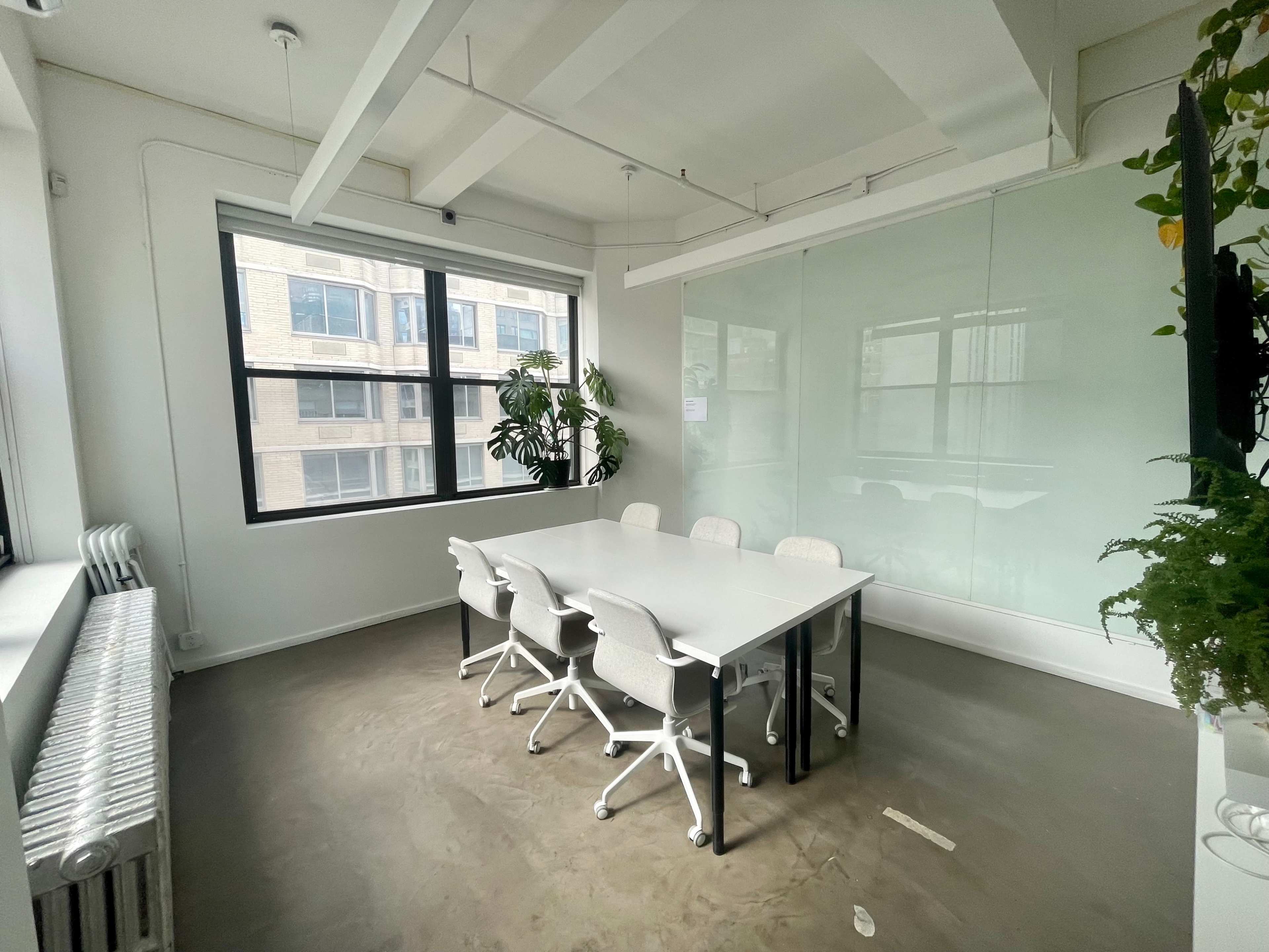 A modern conference room with a white table, ergonomic chairs, and large windows overlooking an exterior view.