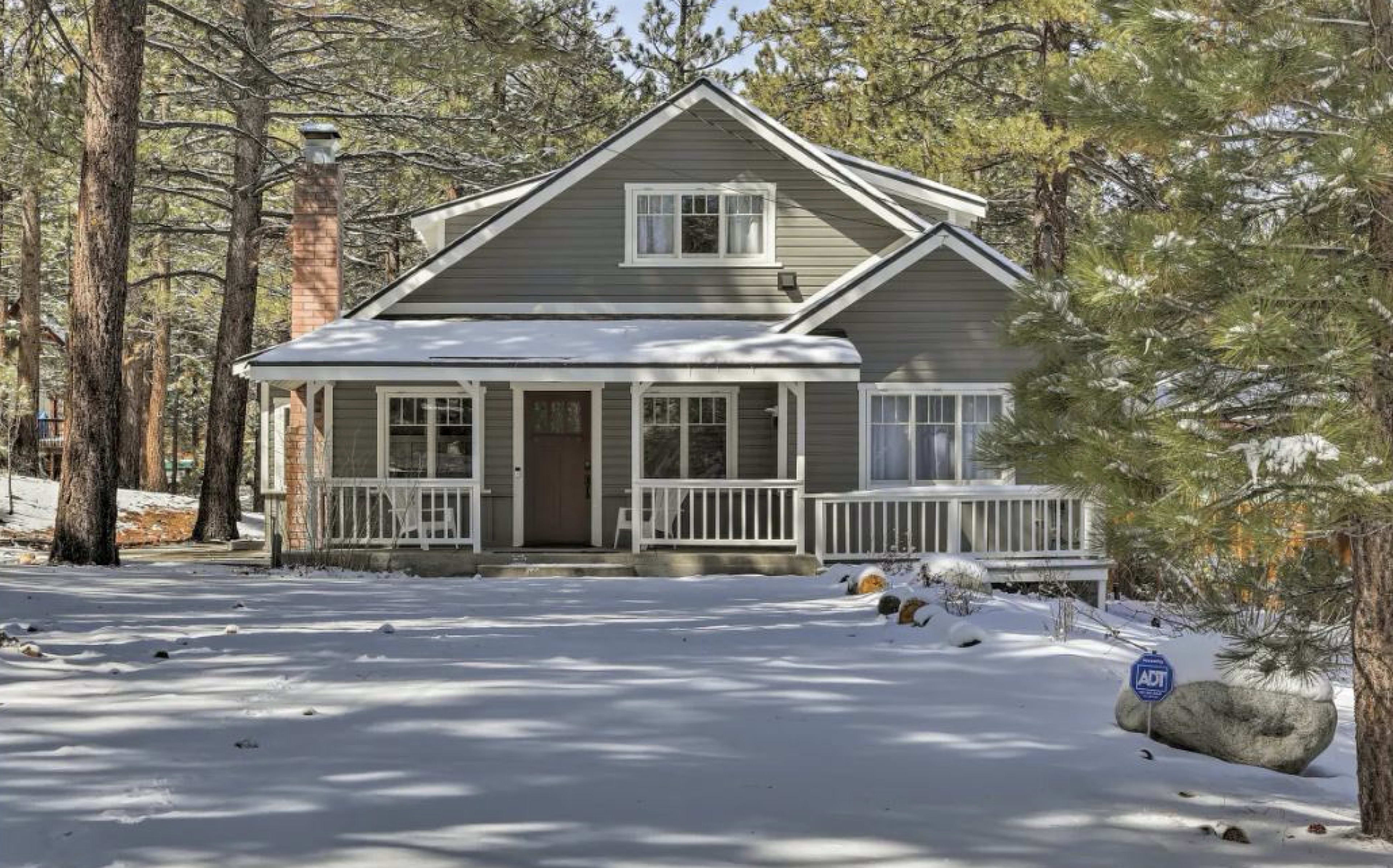 A two-story house with a front porch is surrounded by snow-covered trees.