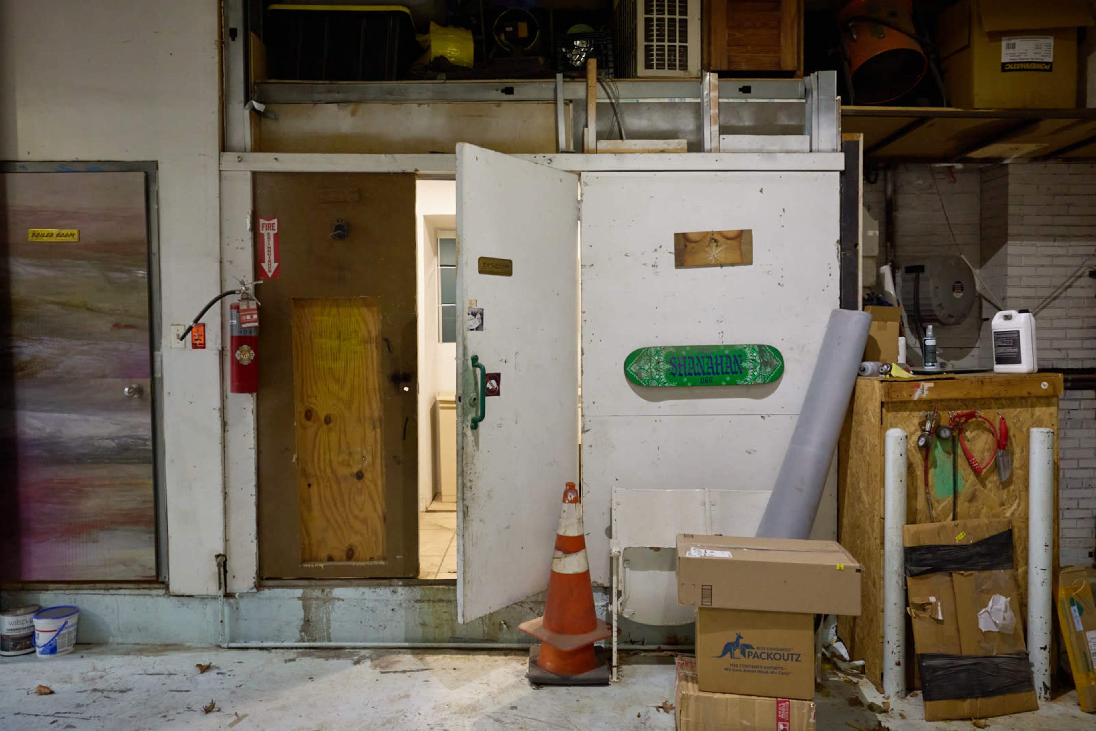 The image shows two doors, one partially open, in a warehouse setting with various equipment and a box on the floor.