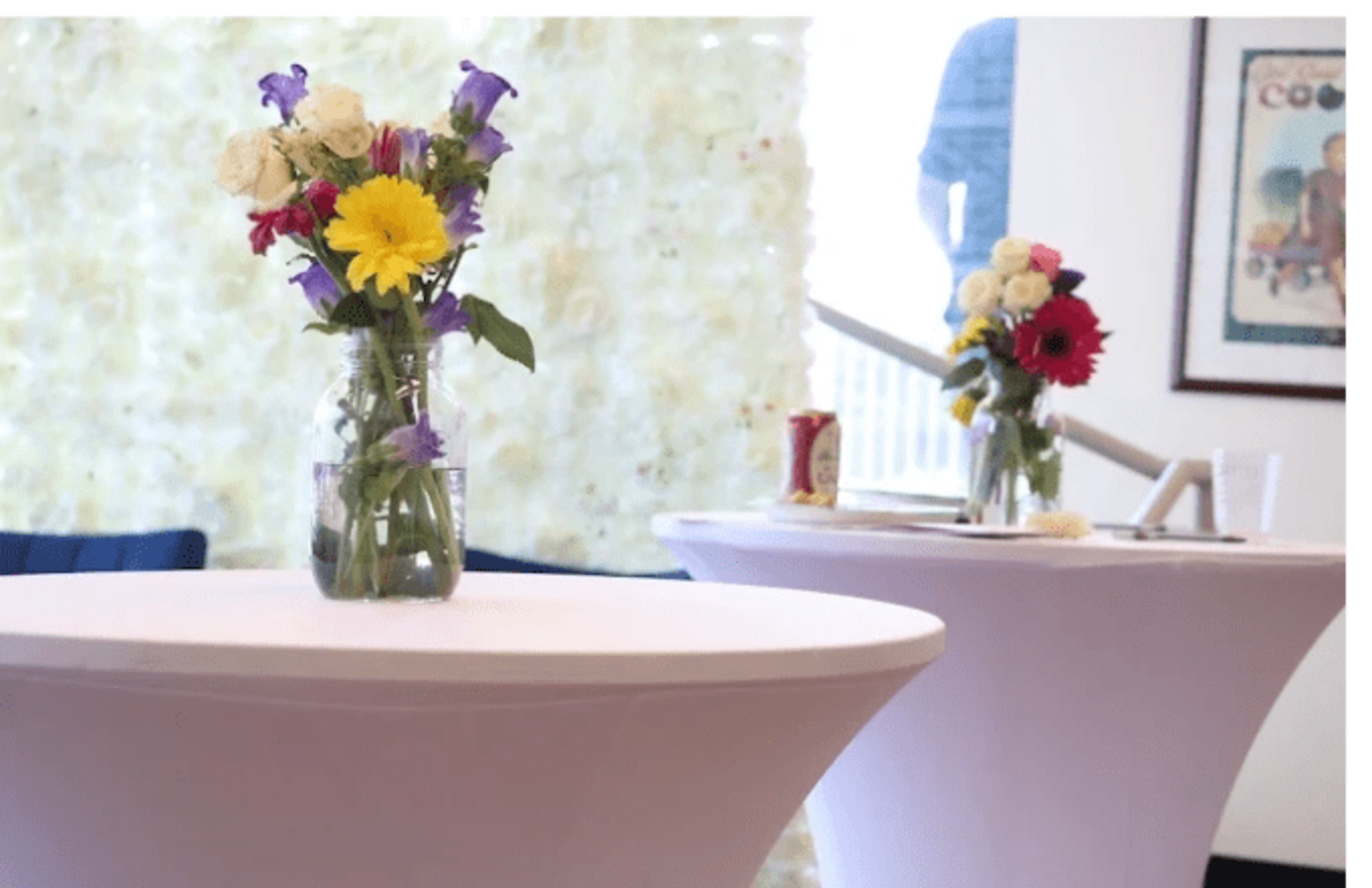 Two tables with floral centerpieces are arranged in a bright indoor setting.