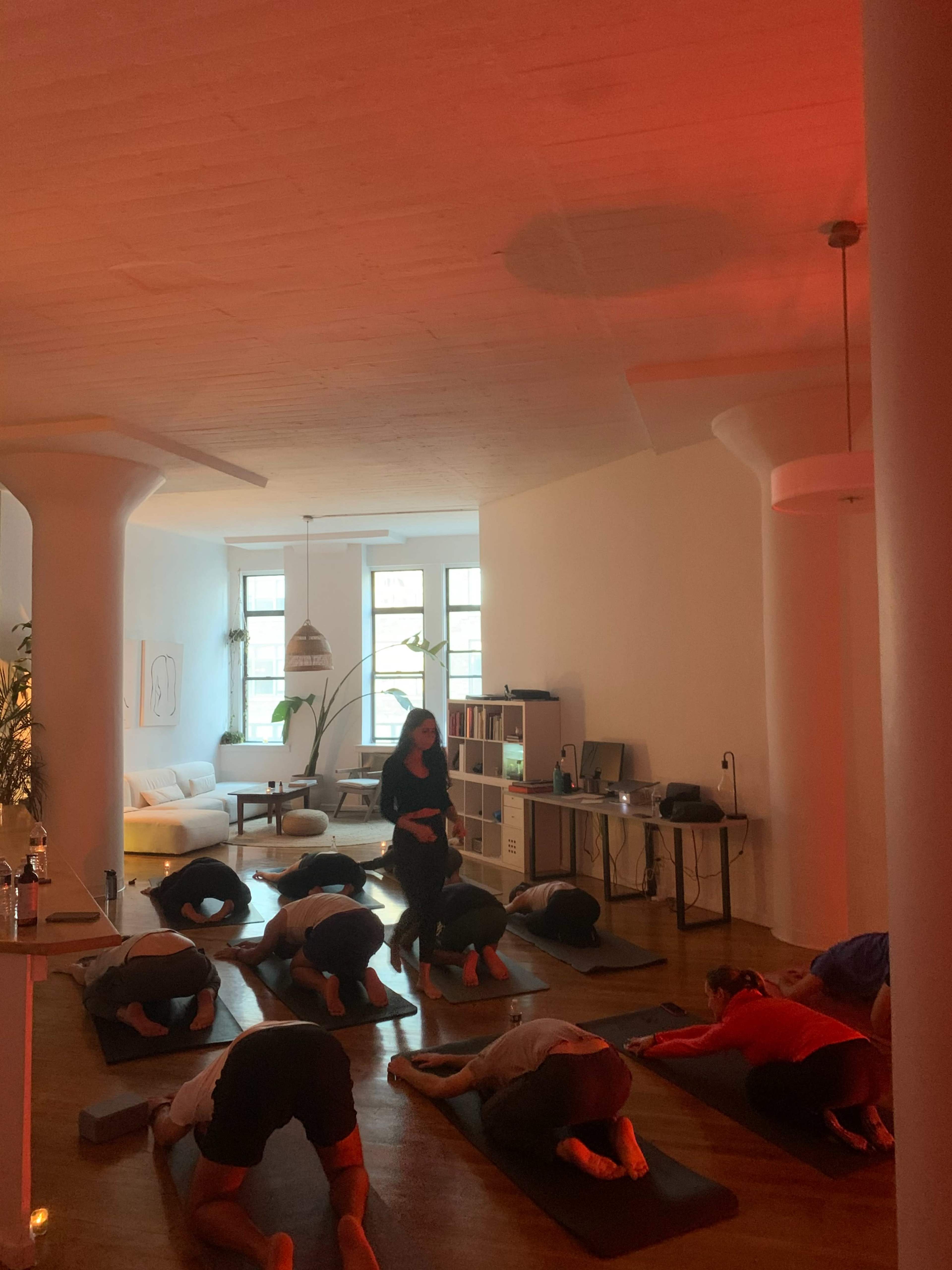 A group of individuals are practicing yoga in a spacious room with large windows and minimalist decor.