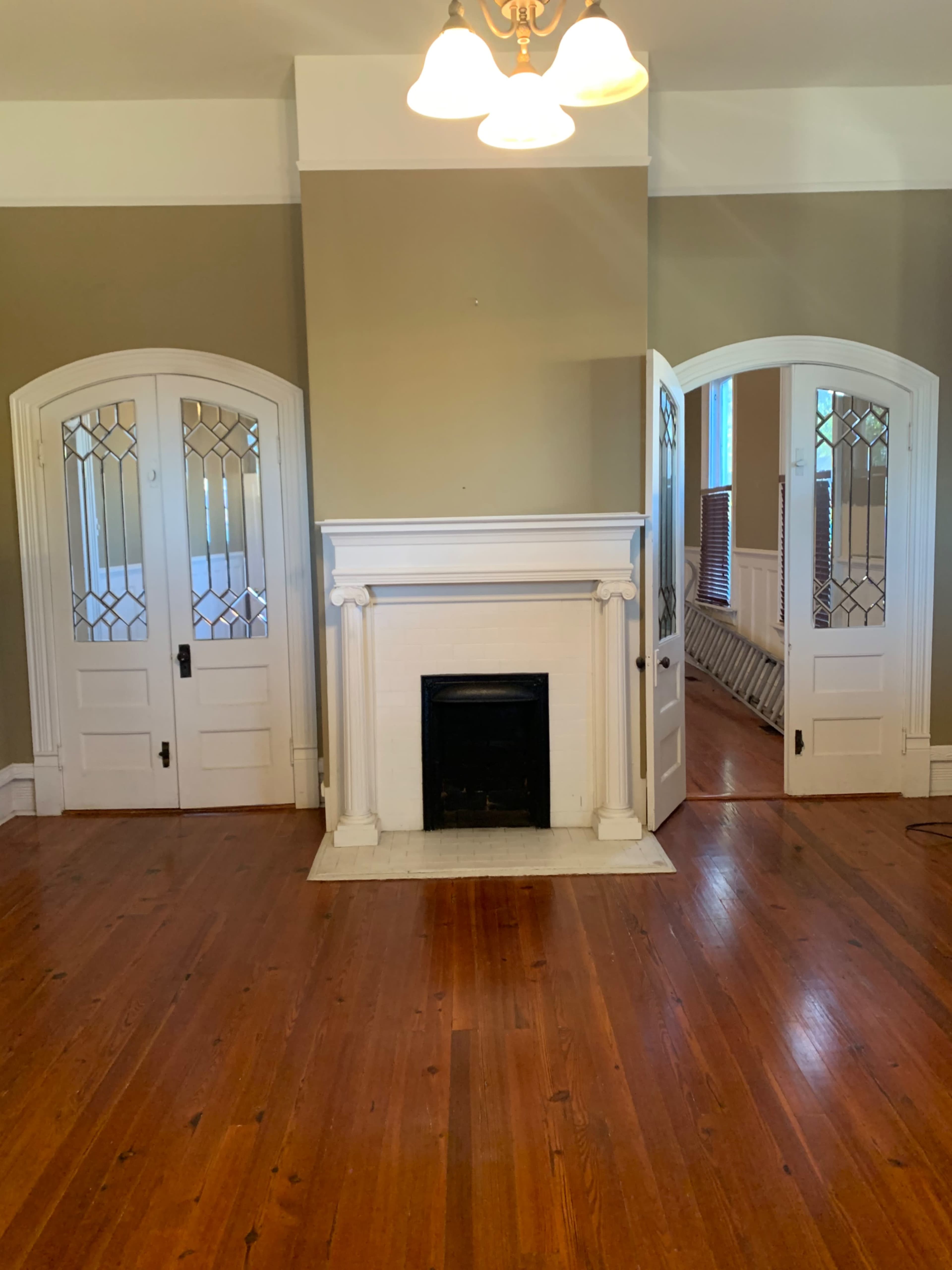 A room with hardwood floors, a central fireplace, and two arched doorways leading to adjacent rooms.