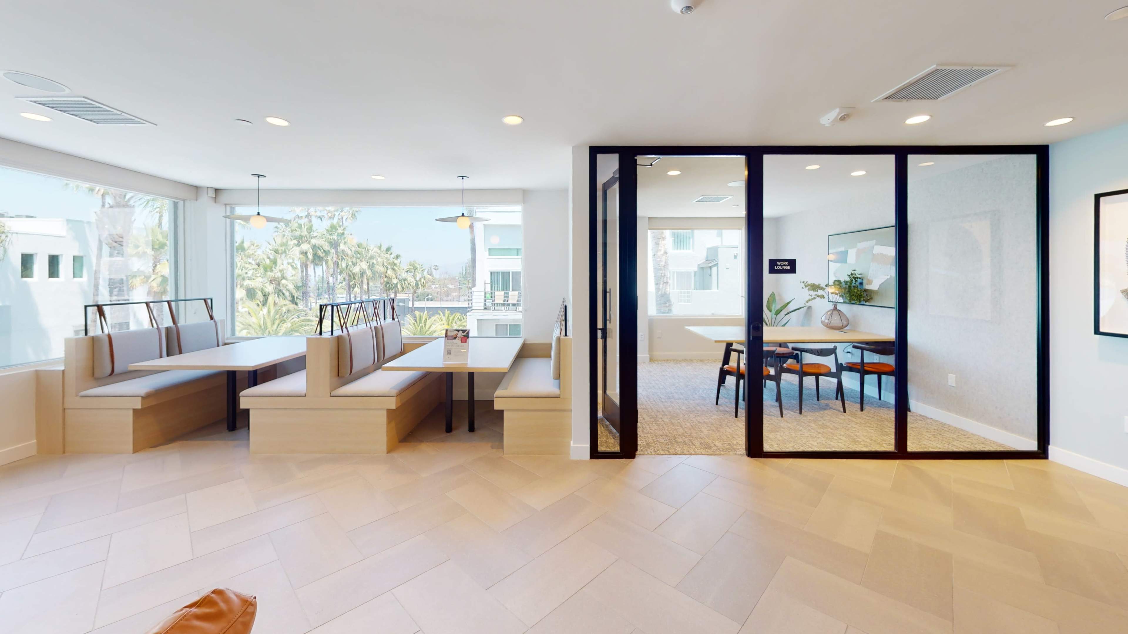 A modern open space featuring a seating area with wooden benches and a glass-walled meeting room adjacent to it.