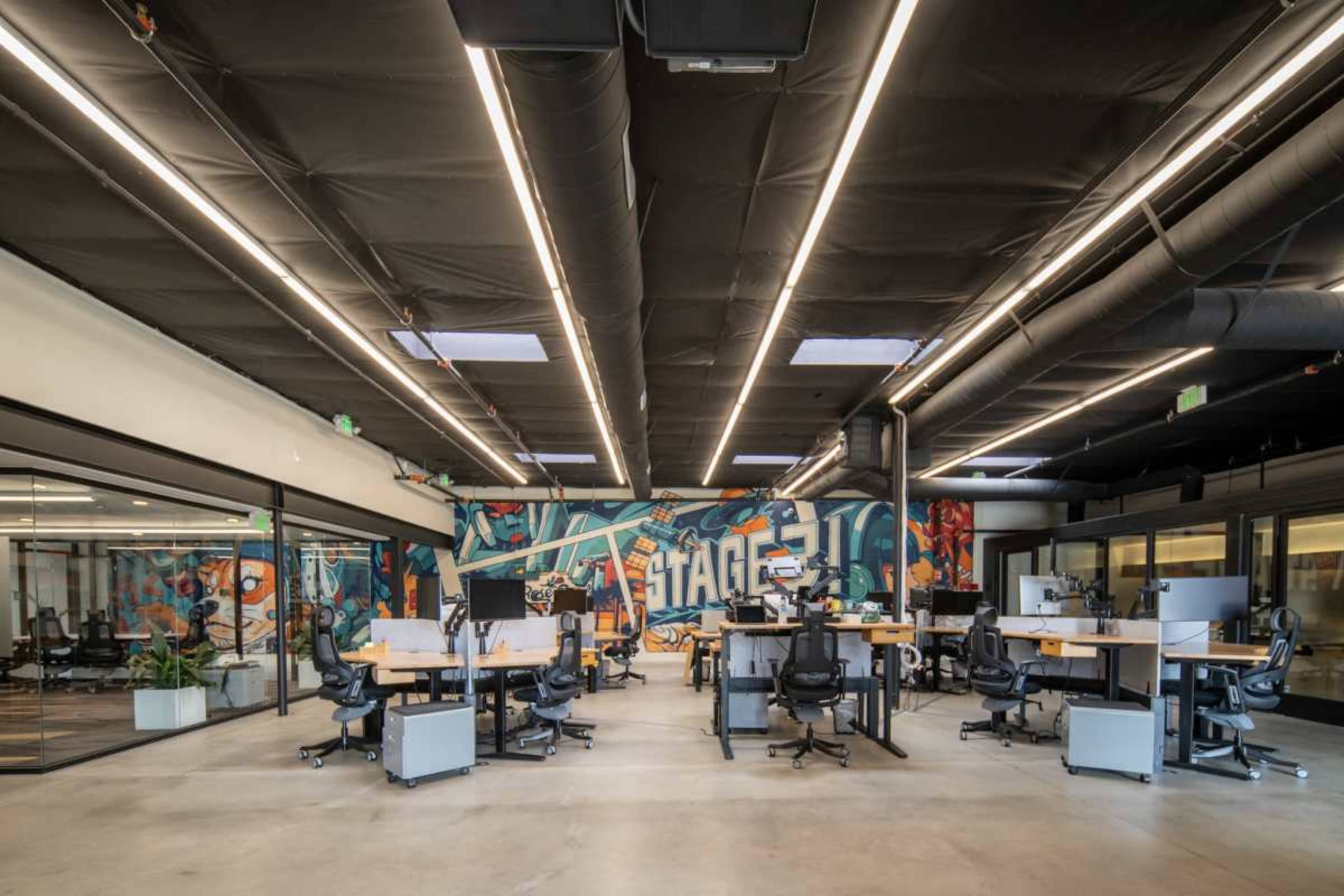 The image shows a modern office interior with multiple desks arranged around a colorful mural on one wall.