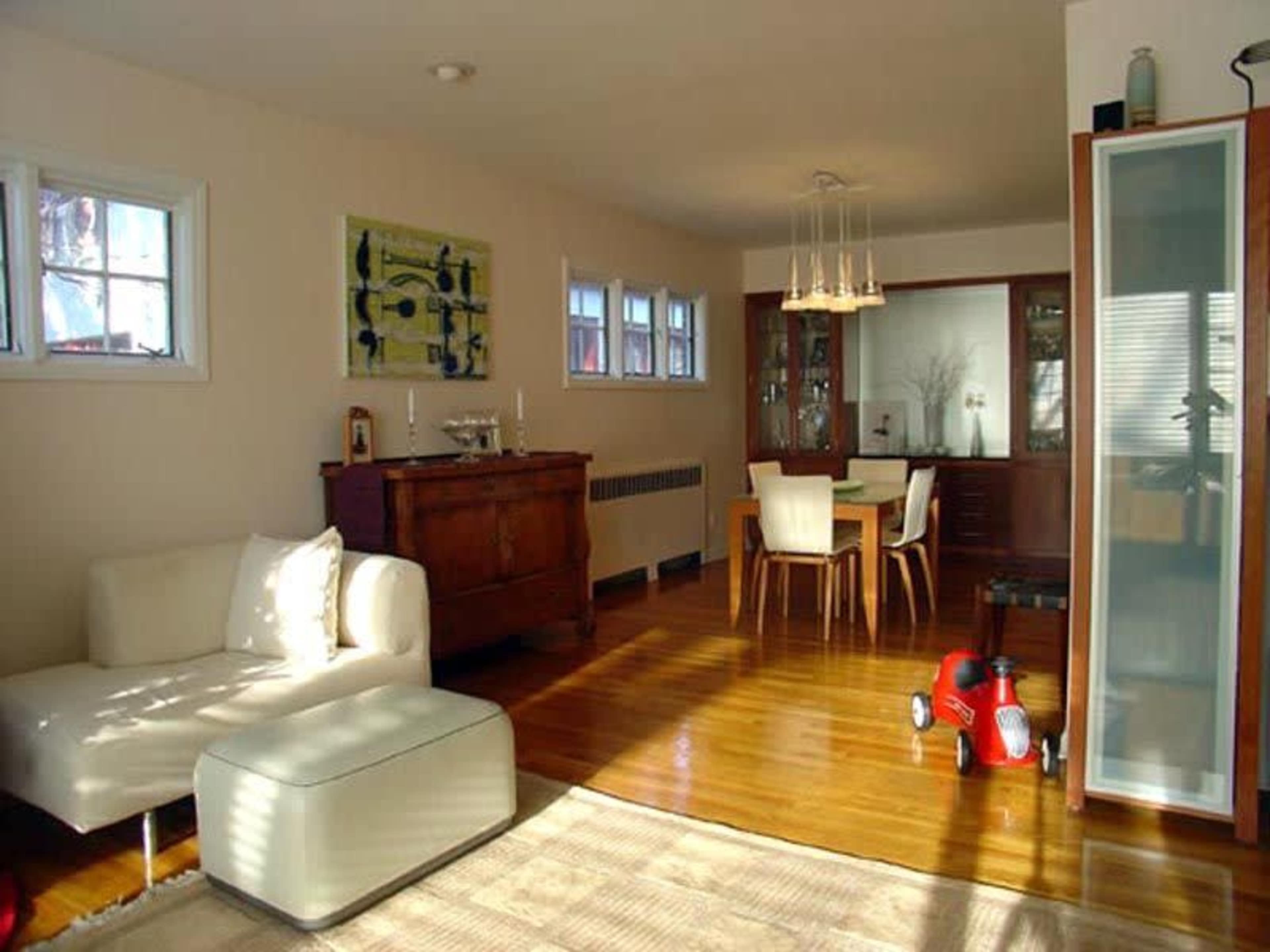 A modern living and dining area featuring a white sofa, a wooden dining table with chairs, and a red toy car on the floor.