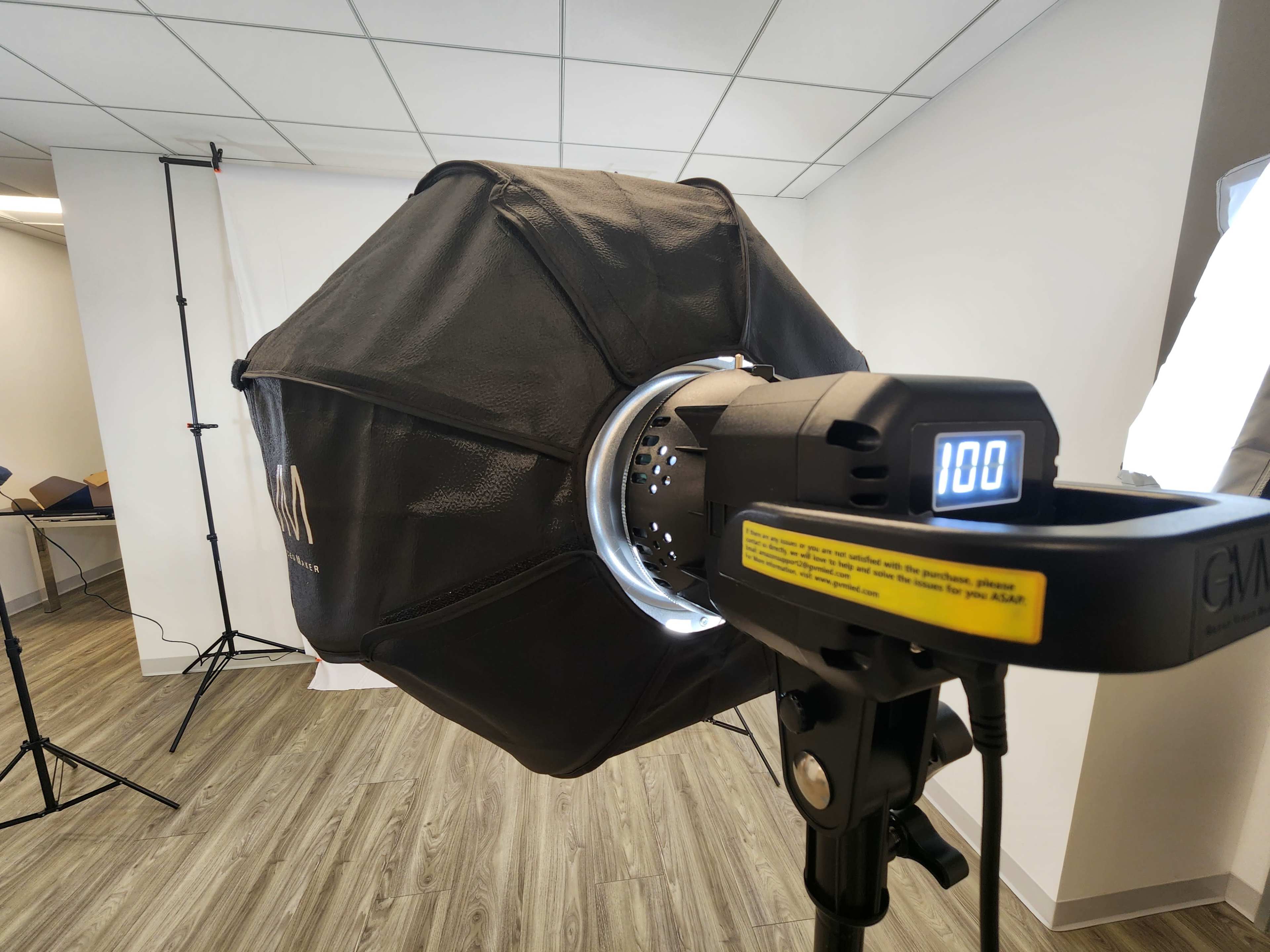 A photography light softbox is positioned in a studio space with backdrop equipment visible in the background.