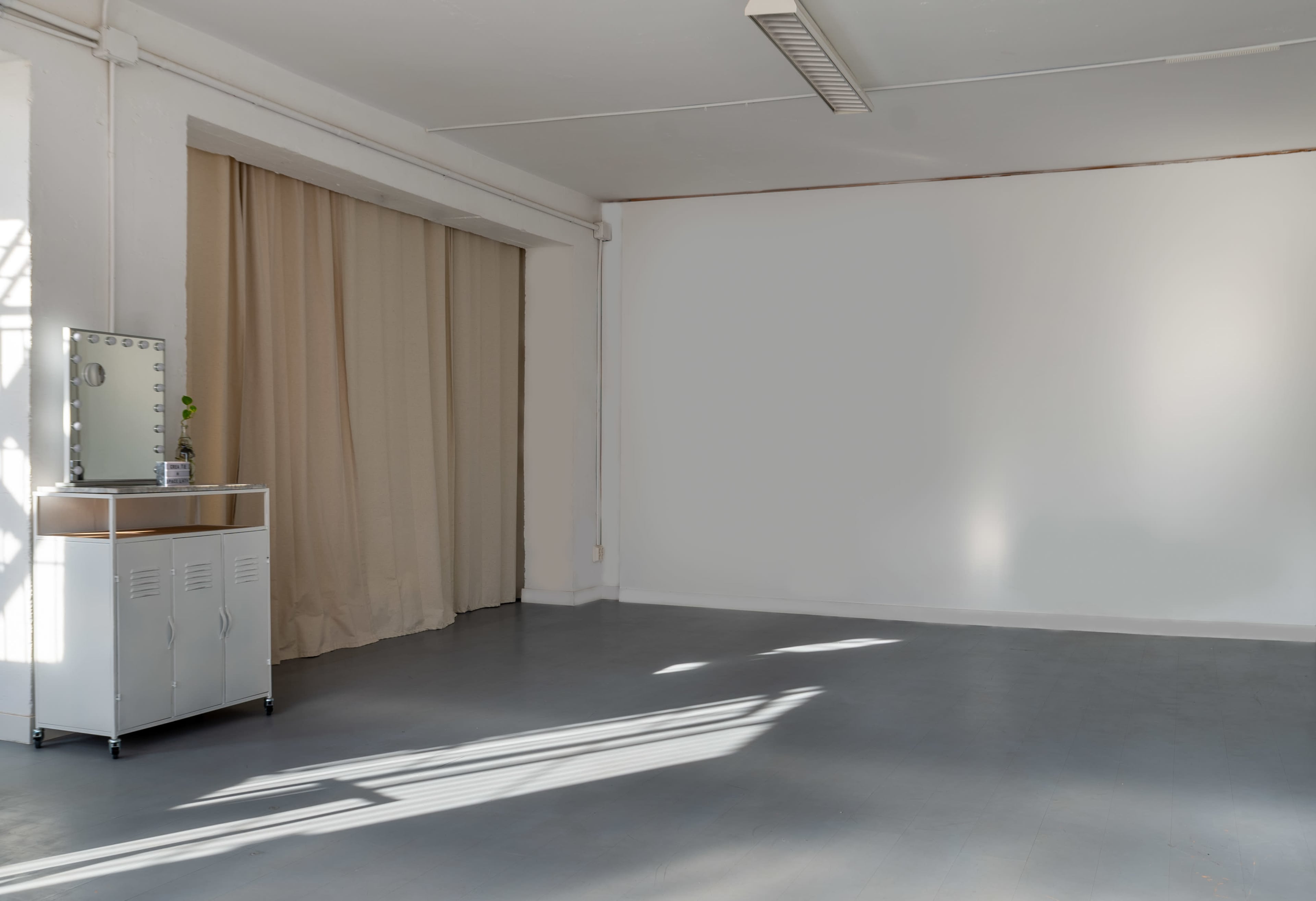 A spacious, empty room with a curtained area and a mirror on a small metal cabinet.