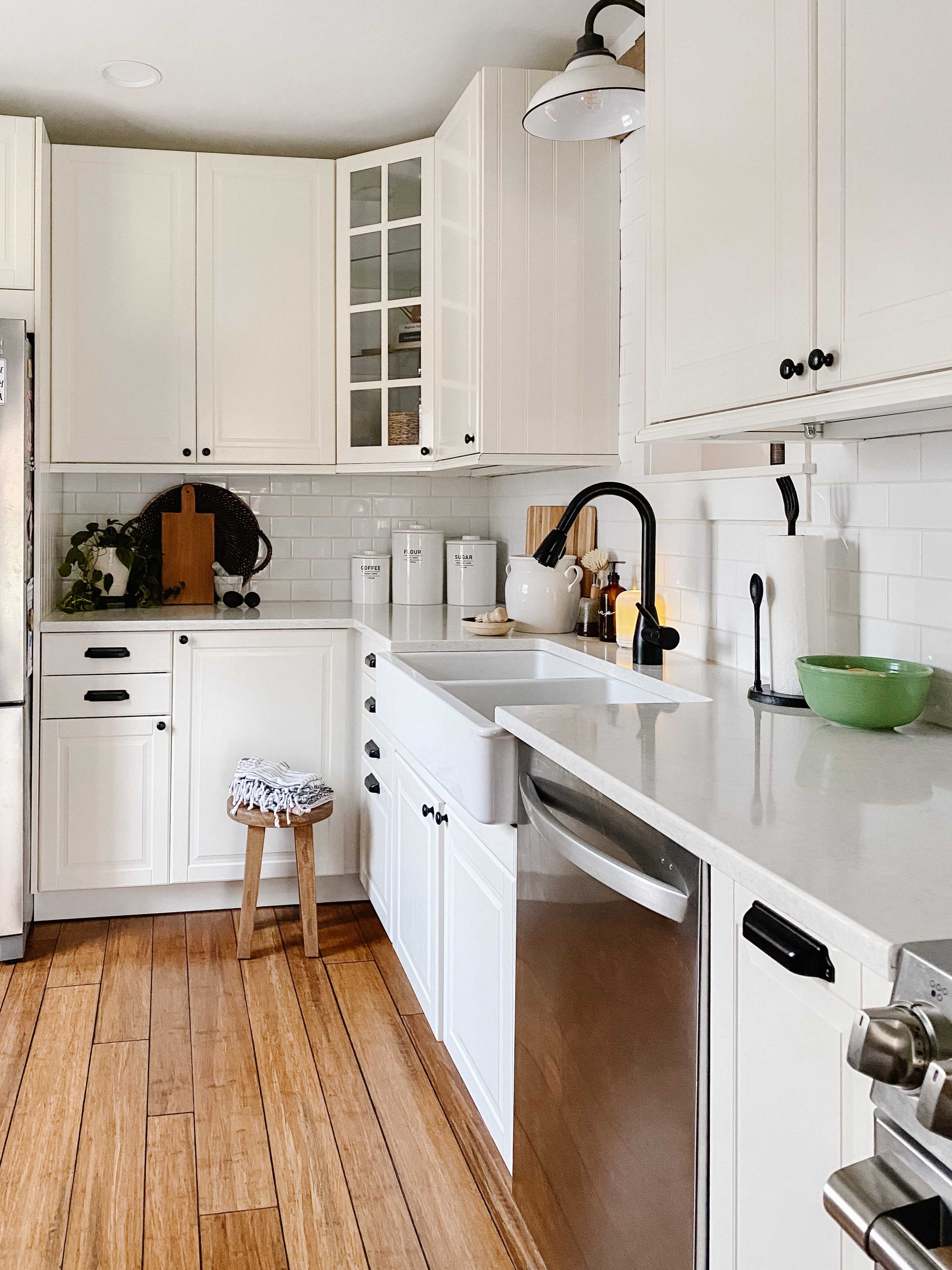 A bright kitchen features white cabinetry, a farmhouse sink, and wooden flooring.