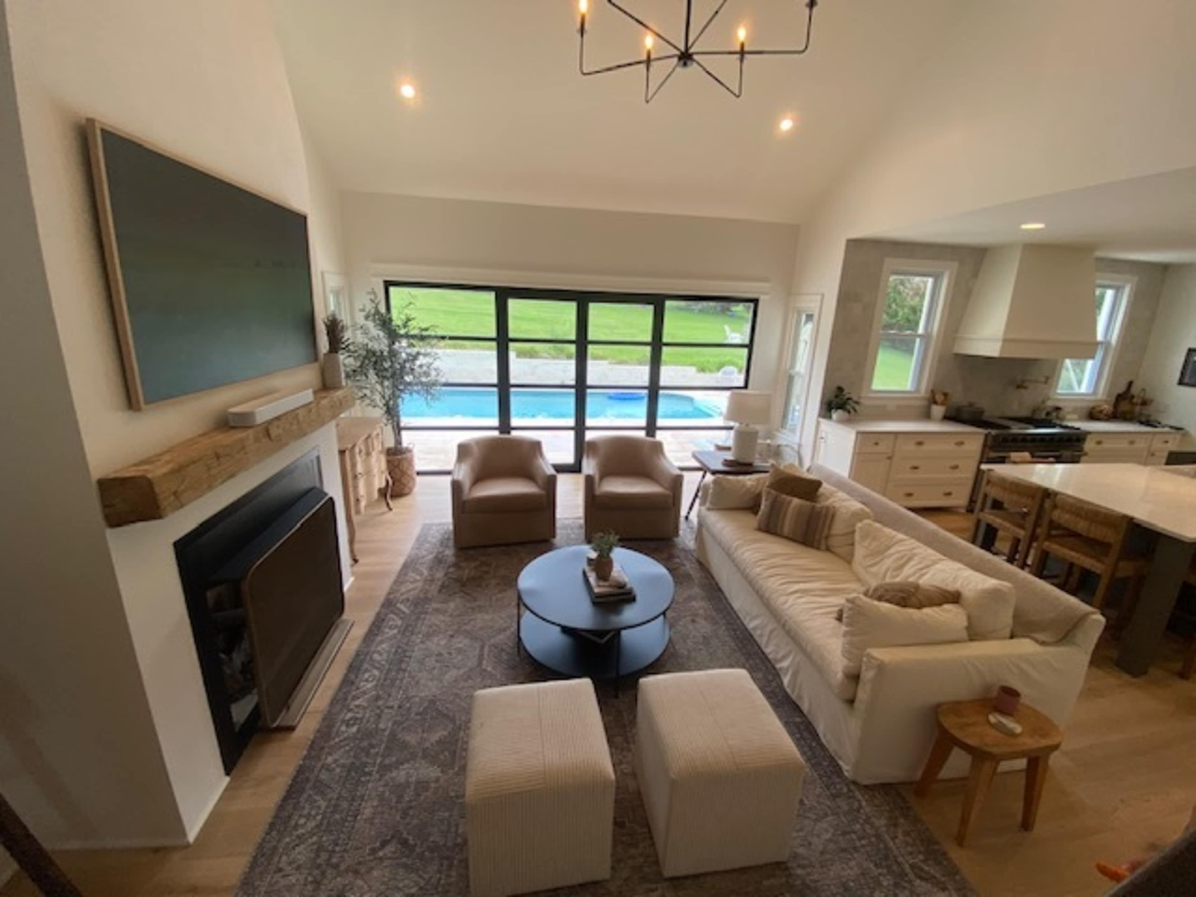 A modern living room with a couch, two armchairs, a coffee table, and an open view of a pool and grassy area through large windows.