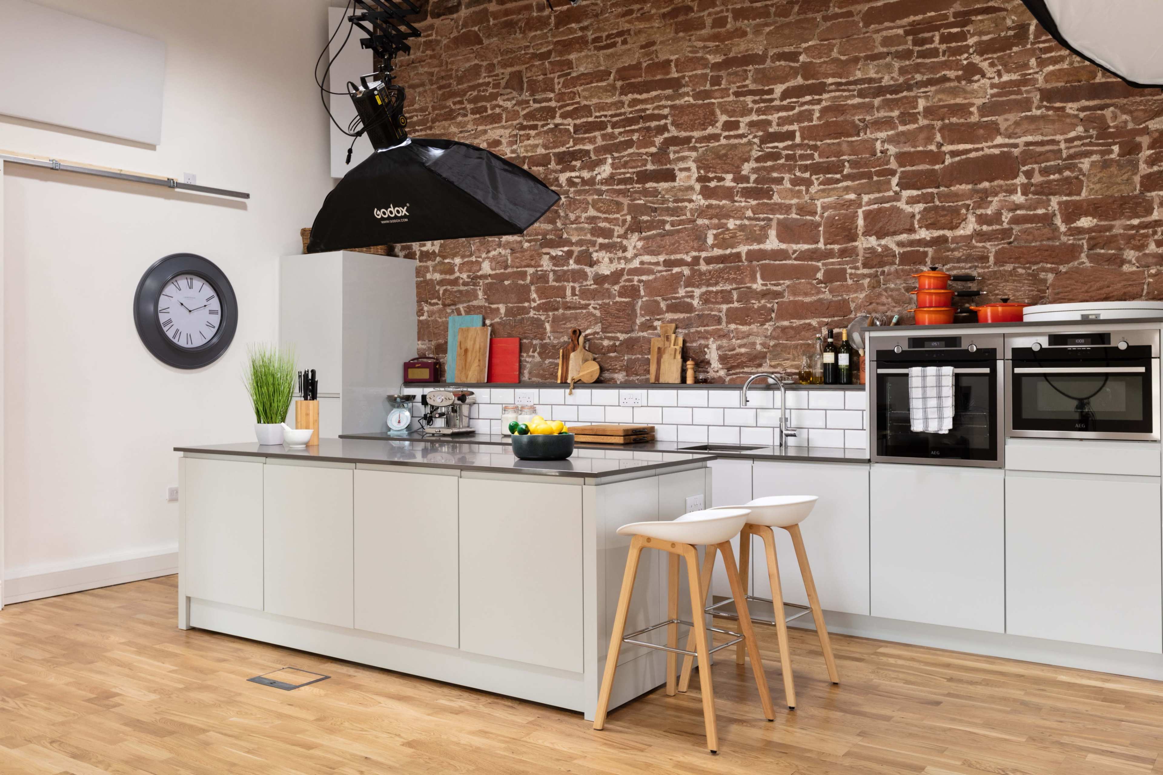 The kitchen features a central island with bar stools, a stone wall, and various cooking utensils displayed on the counter.
