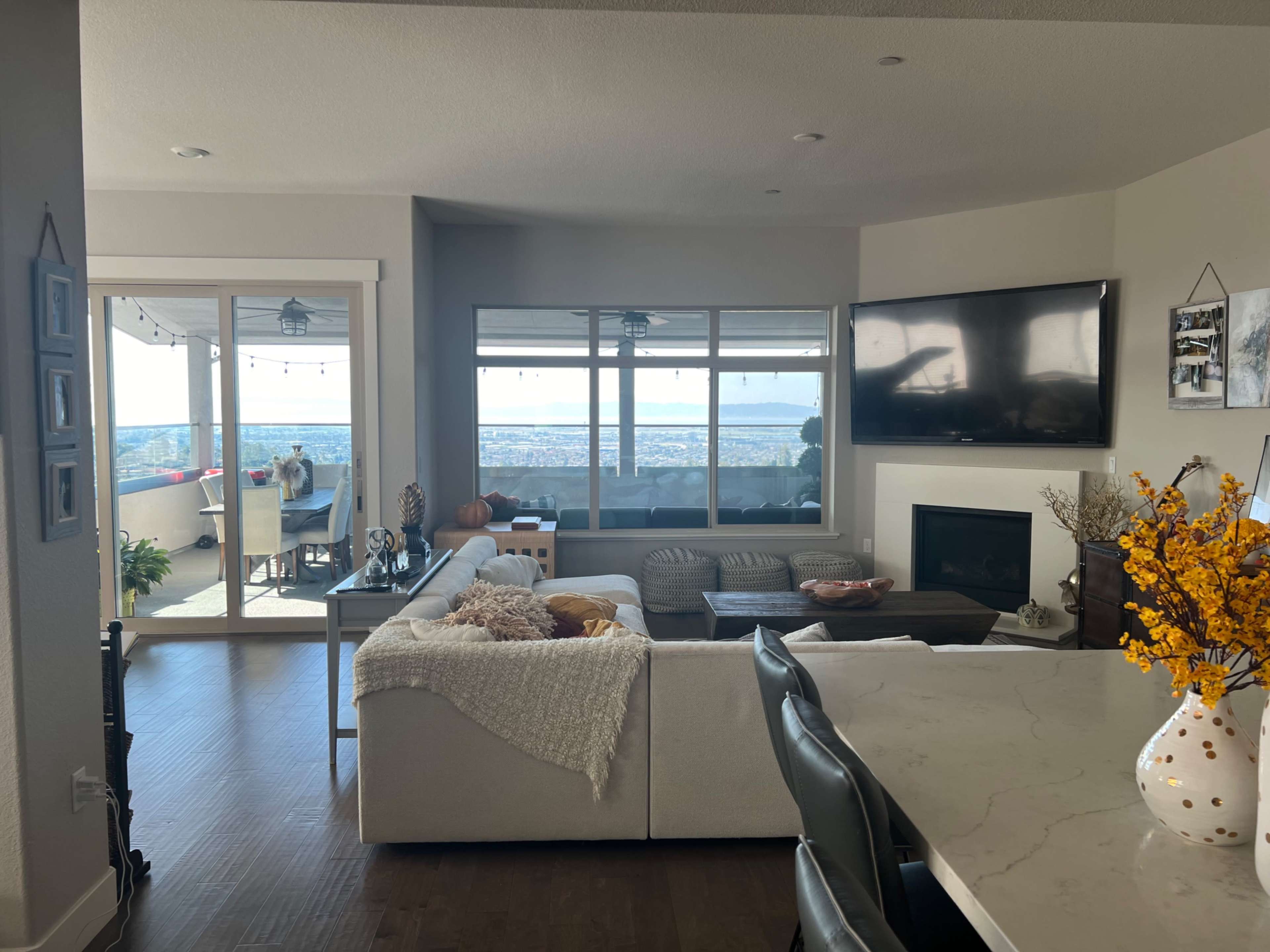A modern living room with a sectional sofa, a coffee table, and a large window offering a view of the outdoors, along with a dining area and a kitchen in the foreground.