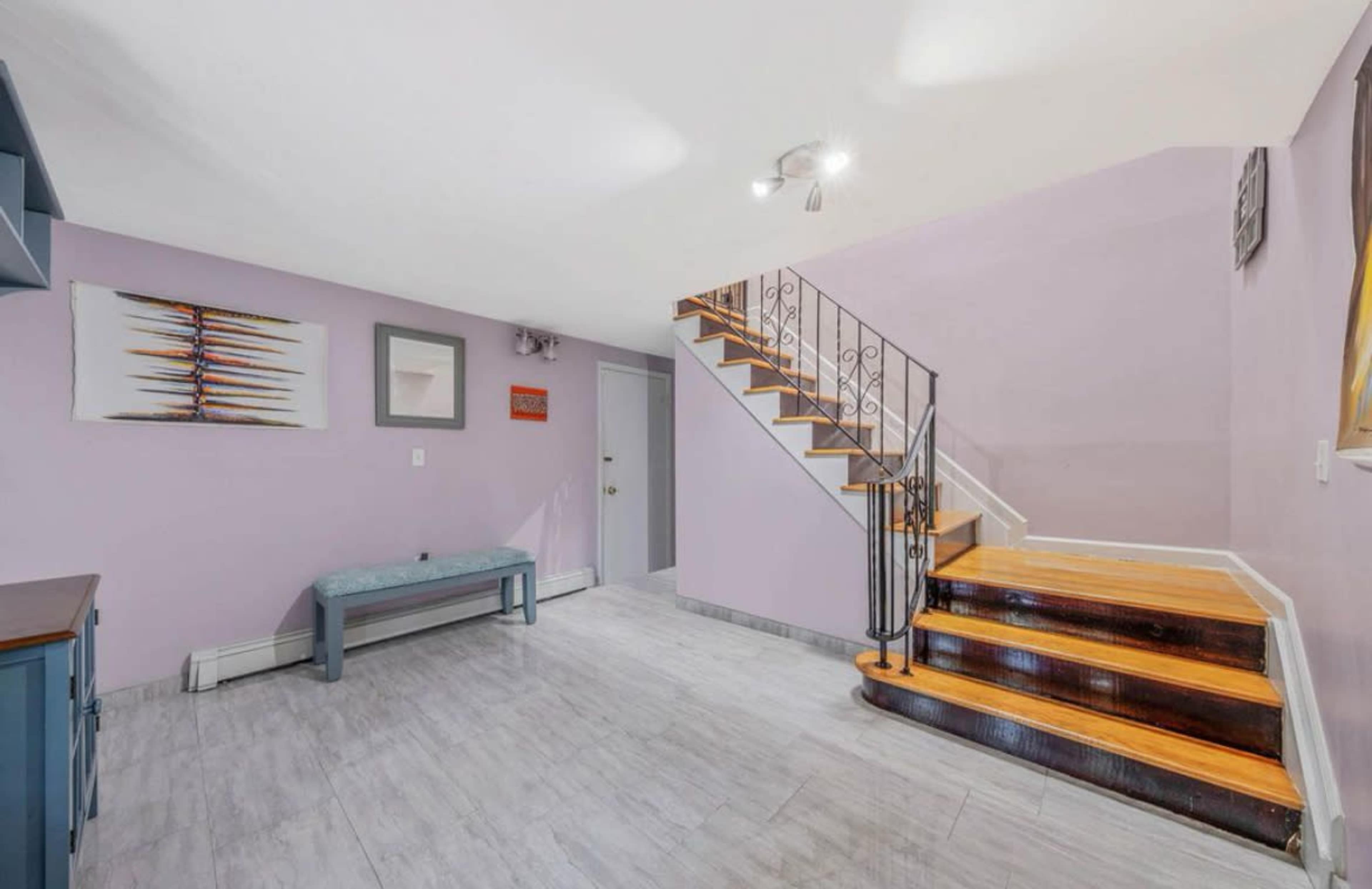 A staircase leads from a purple-walled foyer with tiled flooring, featuring a bench and wall art.