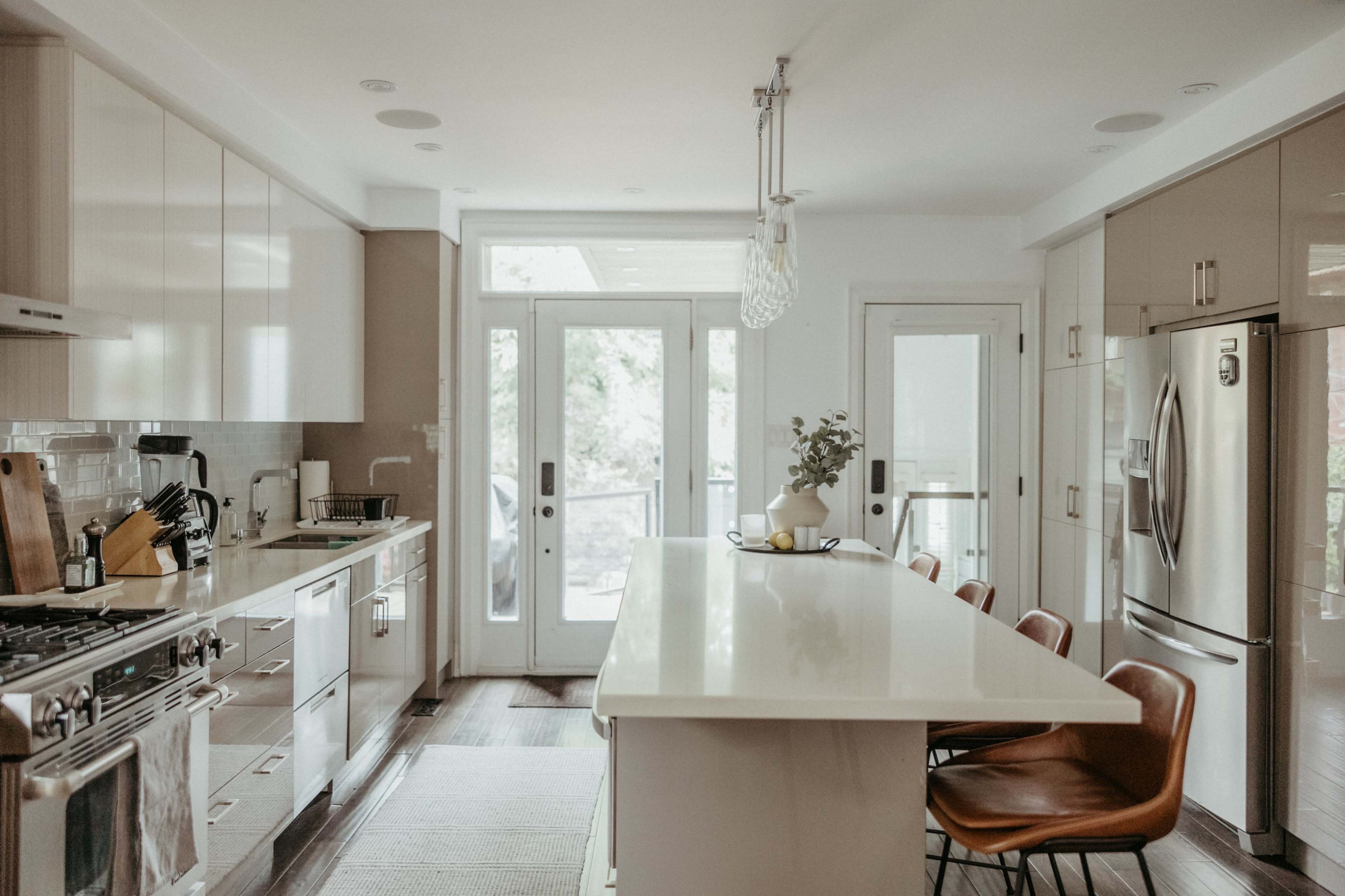 A modern kitchen features a central island with bar stools, stainless steel appliances, and large windows that provide natural light.