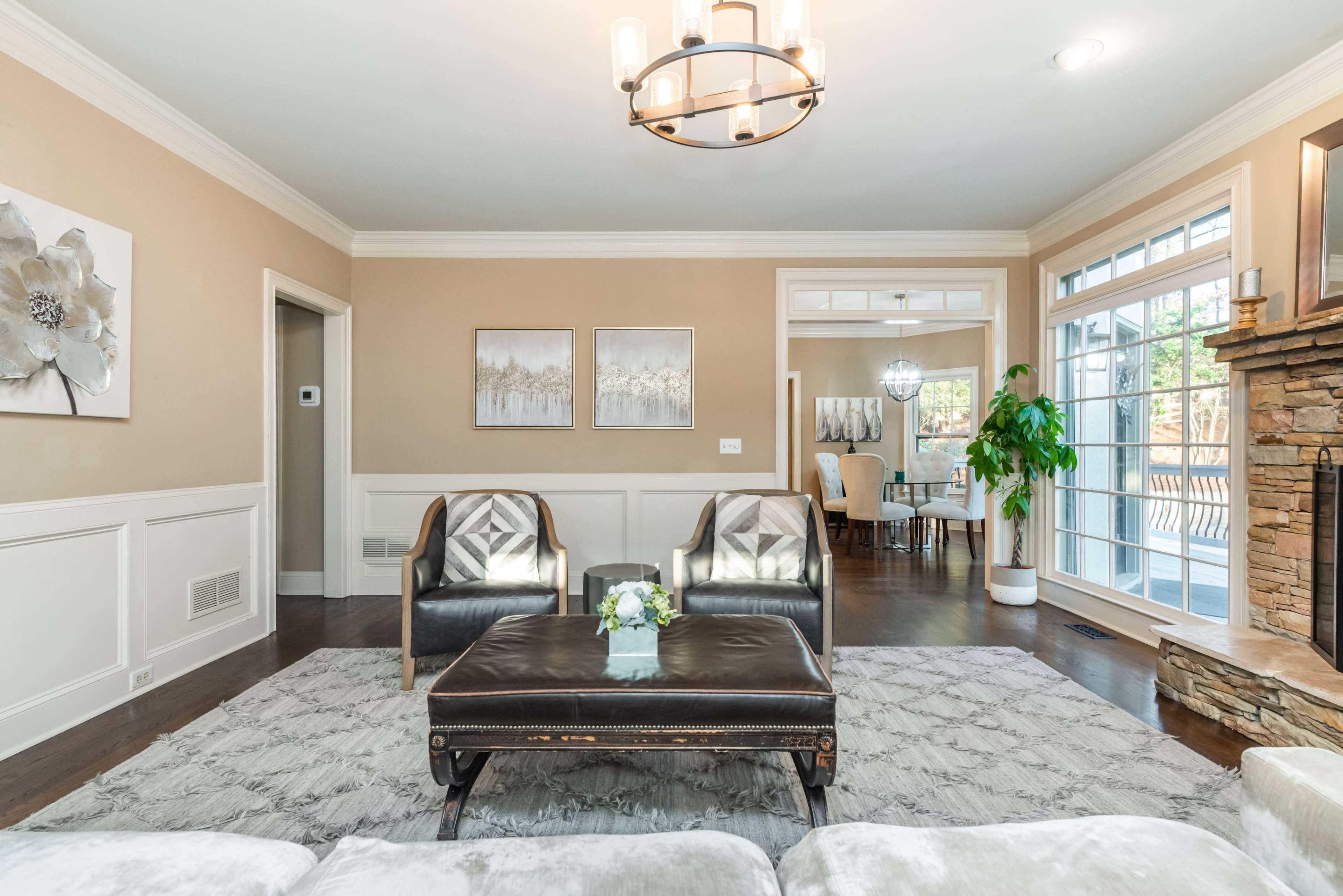 The image shows a living room featuring two armchairs, a coffee table, and a large window that leads to a dining area.