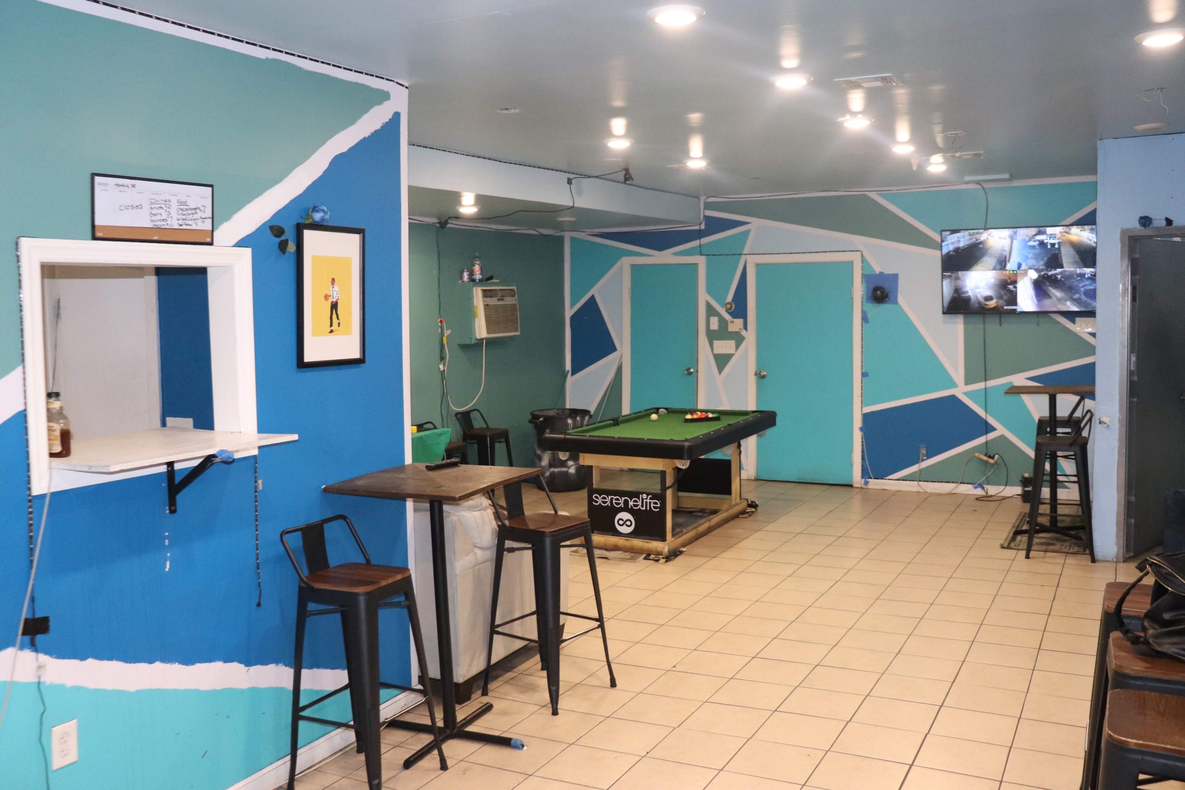 A recreational room with a green pool table, blue and white geometric wall decor, and a wall-mounted TV displaying surveillance footage.