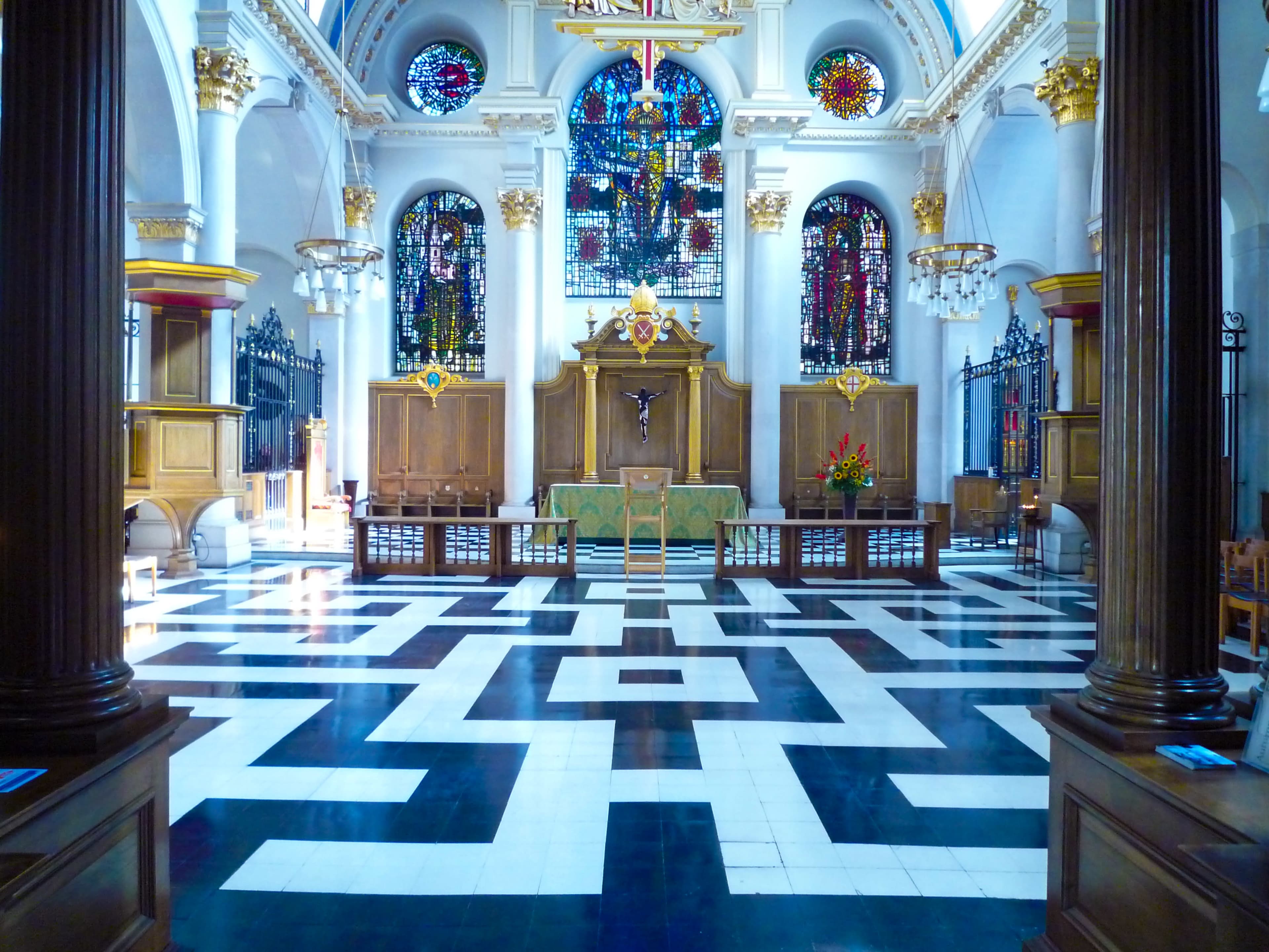 The interior of a church features a patterned floor, wooden pews, and stained glass windows depicting religious scenes.