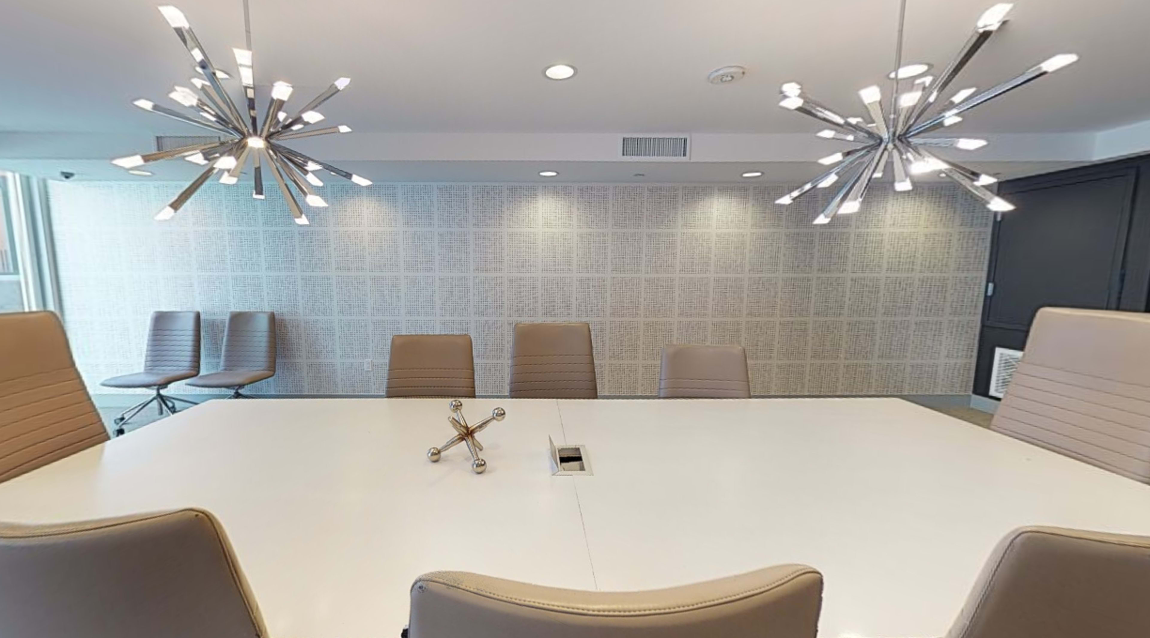 A modern conference room with a large white table, ergonomic chairs, and stylish light fixtures hanging from the ceiling.