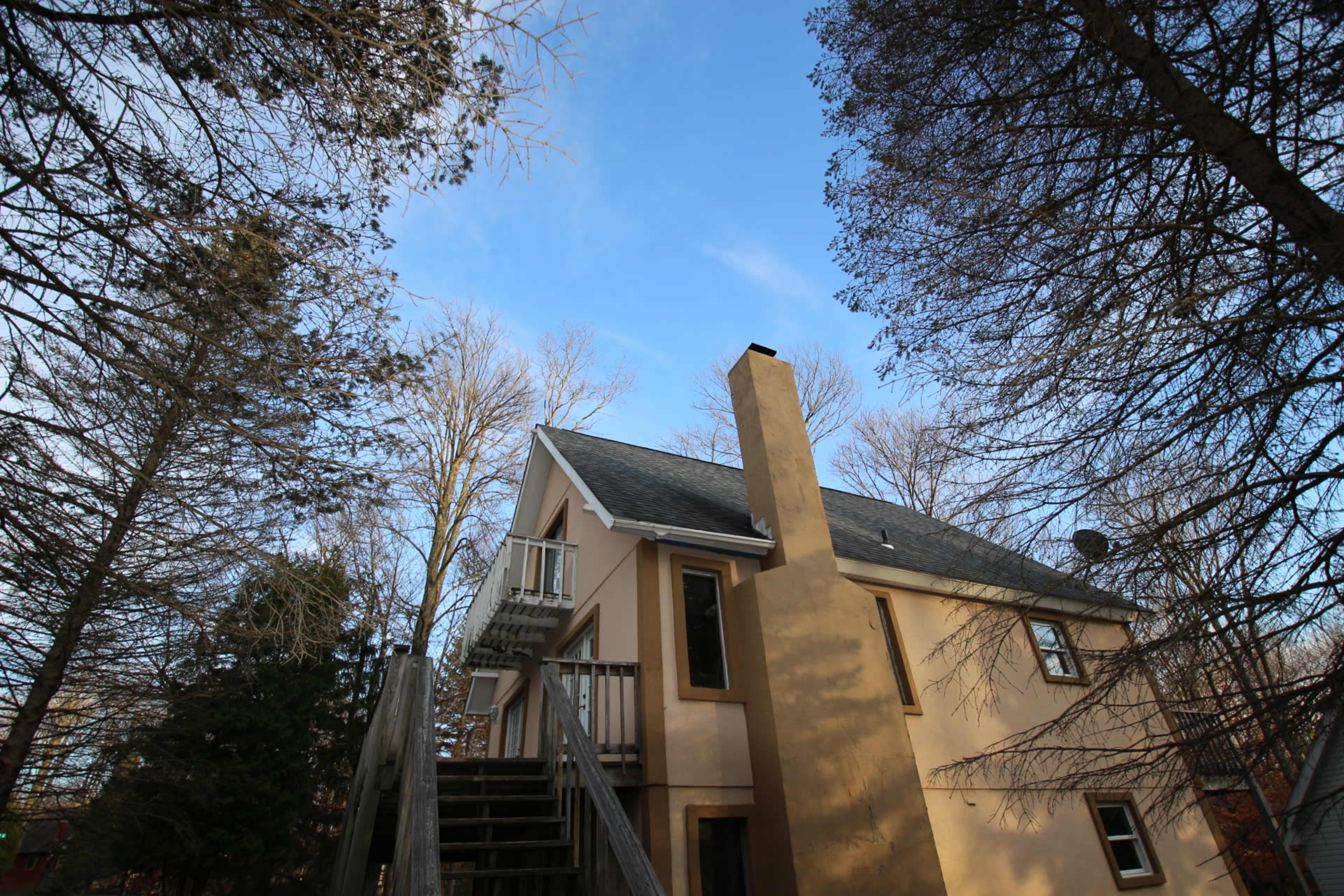 The image shows a two-story house surrounded by bare trees under a clear blue sky.