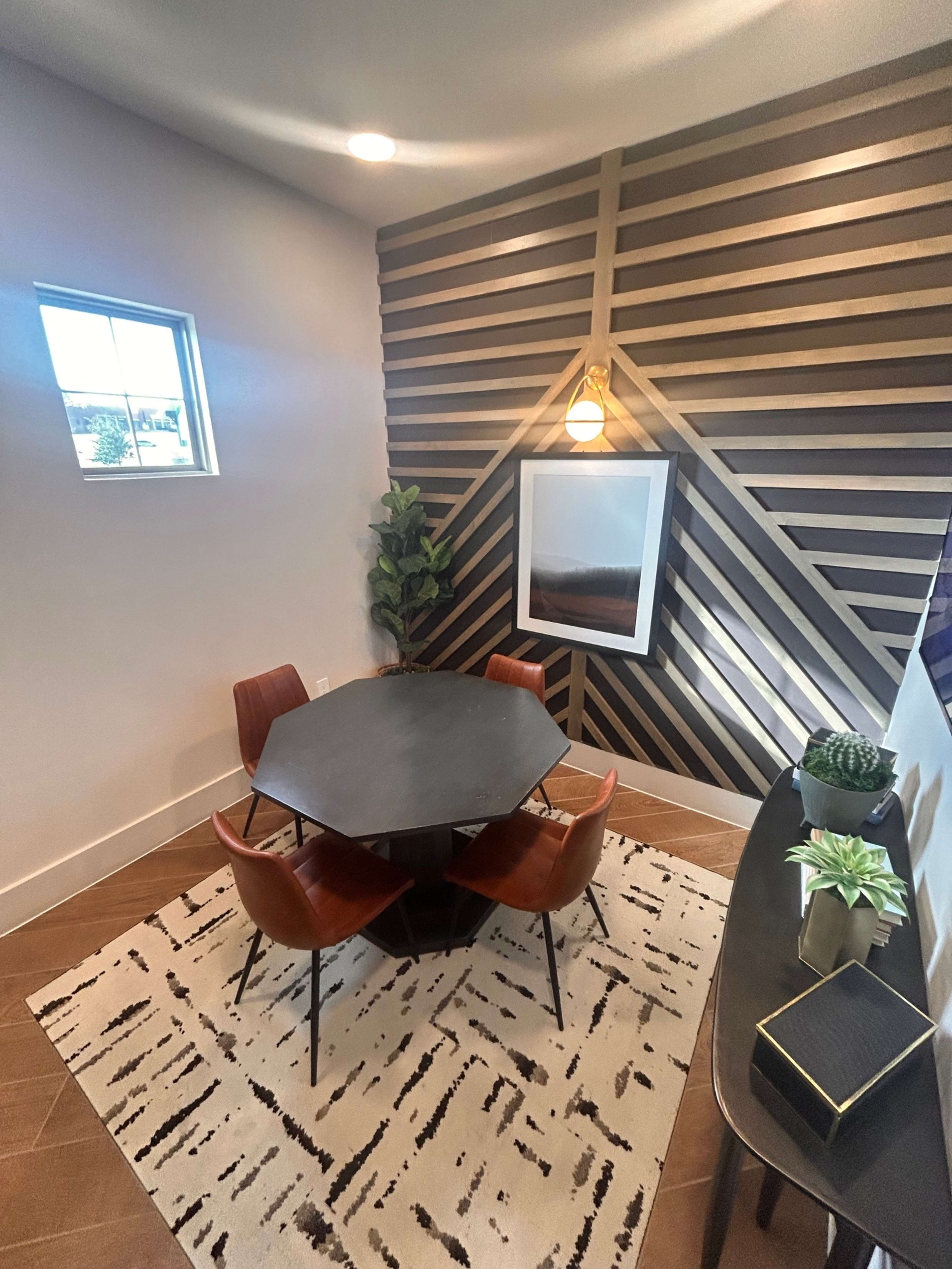 A small dining area features an octagonal black table surrounded by four wooden chairs, with a striped accent wall and a window letting in natural light.