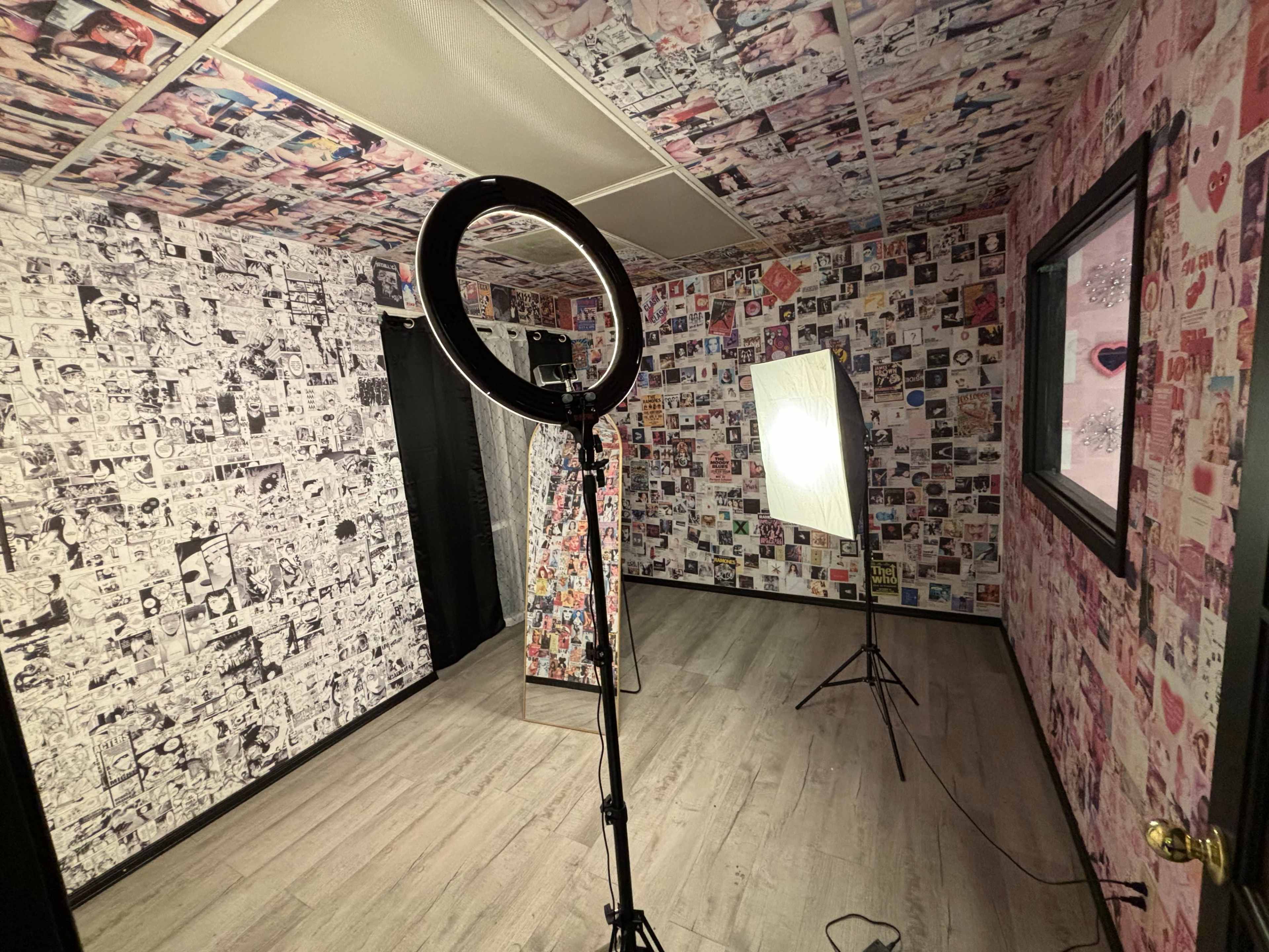 The image shows a small room with walls covered in black-and-white photographs and a ring light set up alongside a softbox lighting equipment.