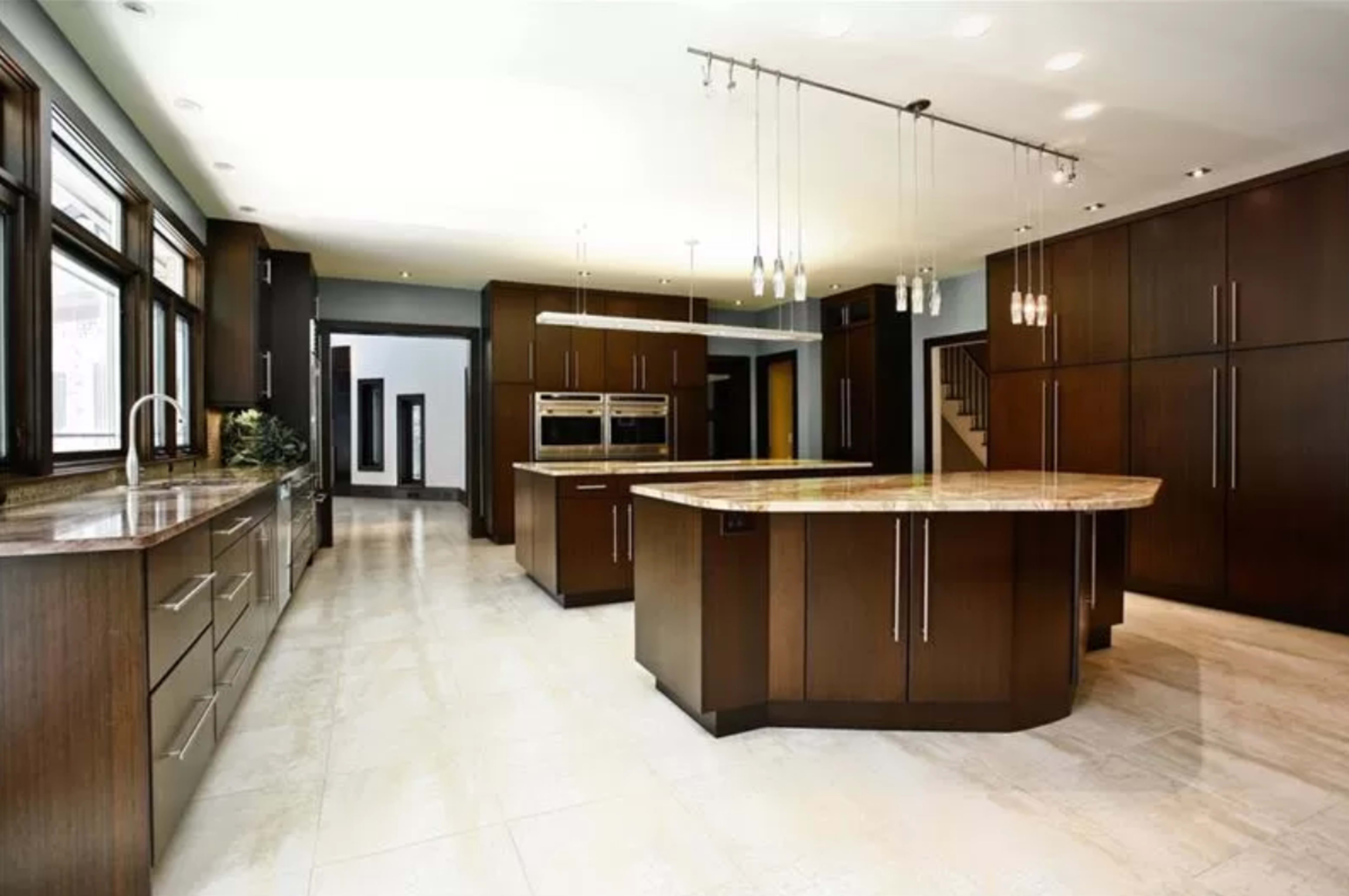 A modern kitchen featuring dark wooden cabinetry, a large central island with a marble countertop, and several pendant lights hanging from the ceiling.
