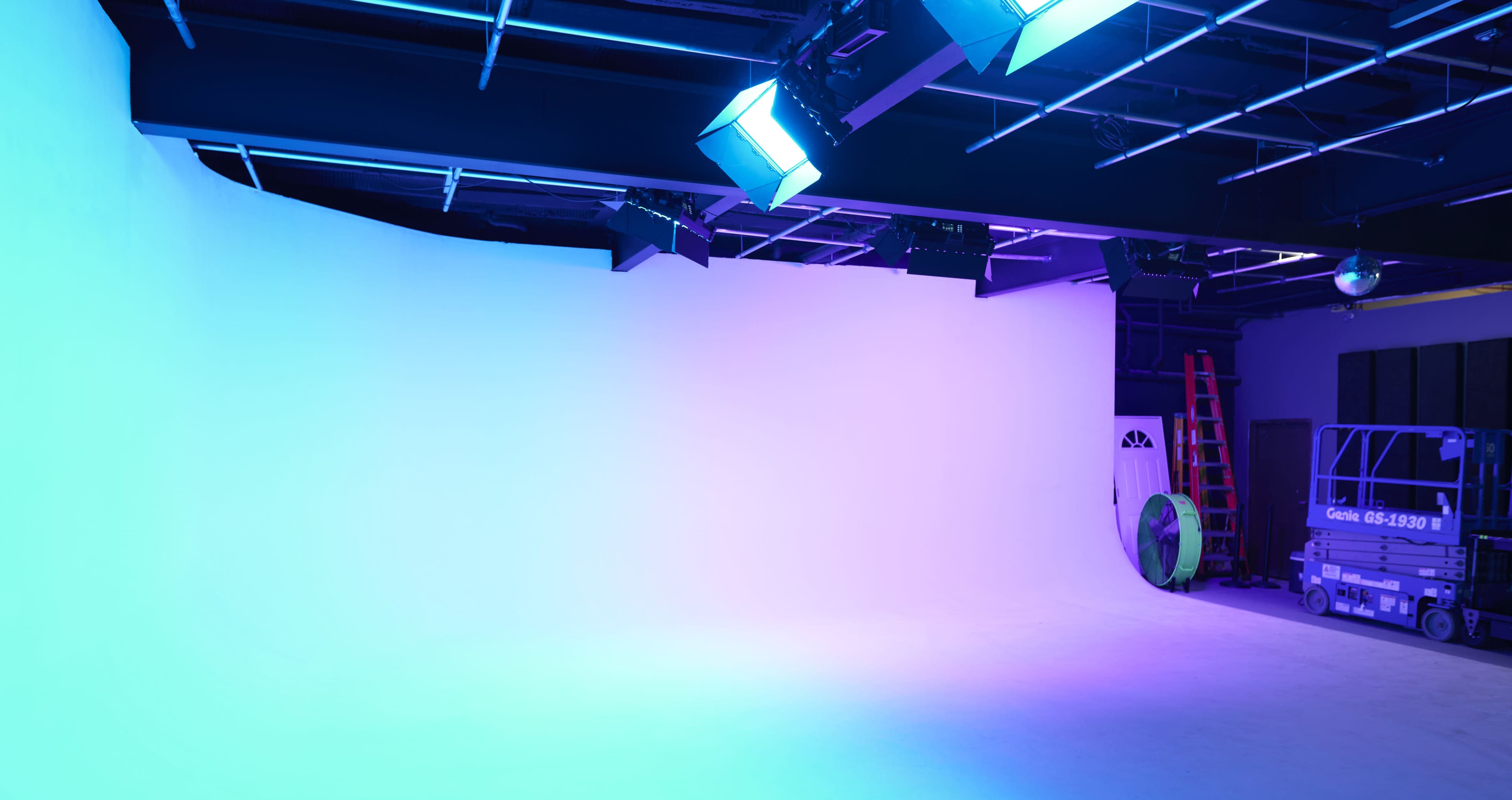 A spacious, lit studio with a large seamless backdrop and equipment, including lights and a ladder.