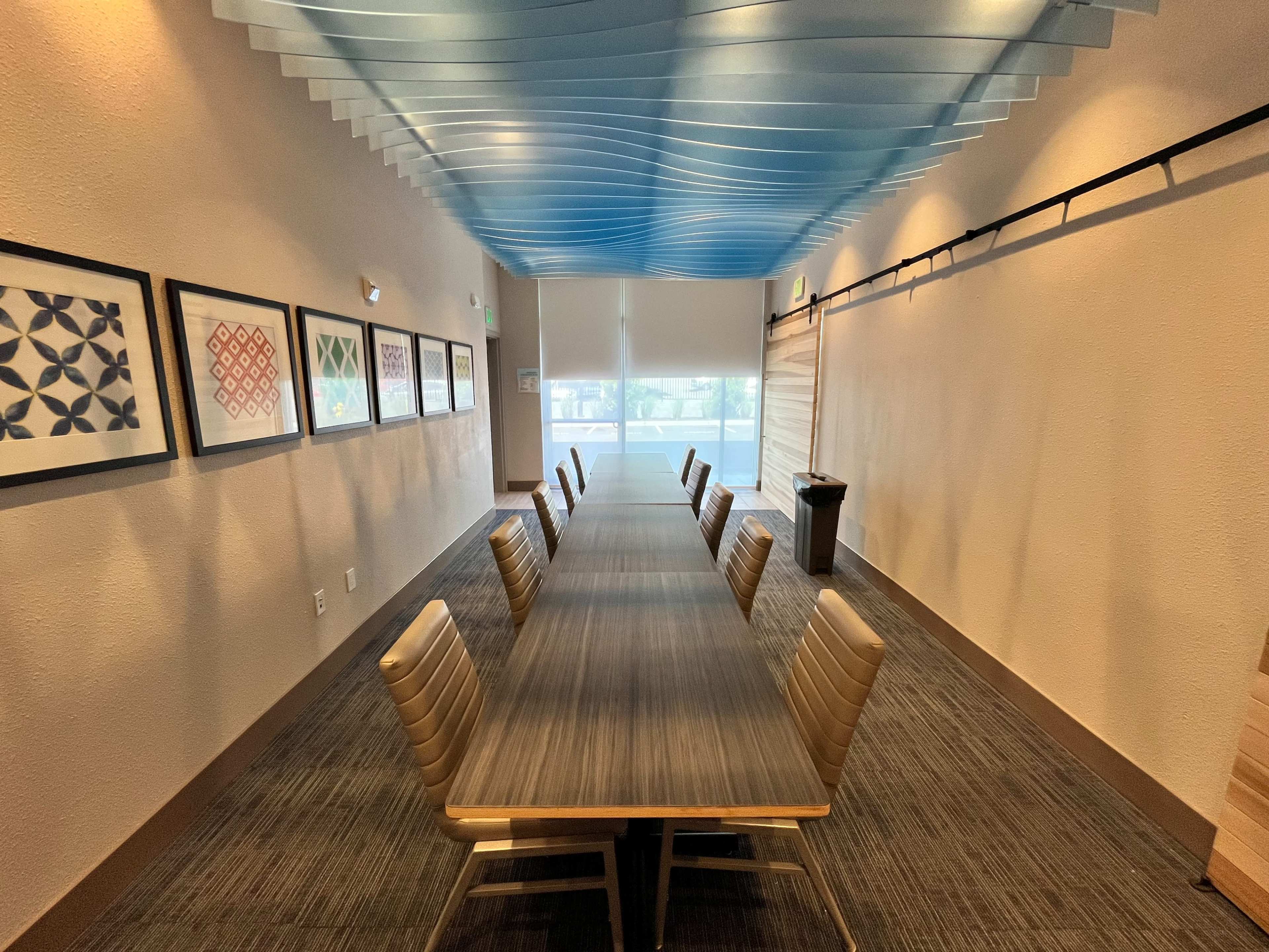 The image shows a long, empty conference room with a large table and several chairs, flanked by framed artwork on the walls.