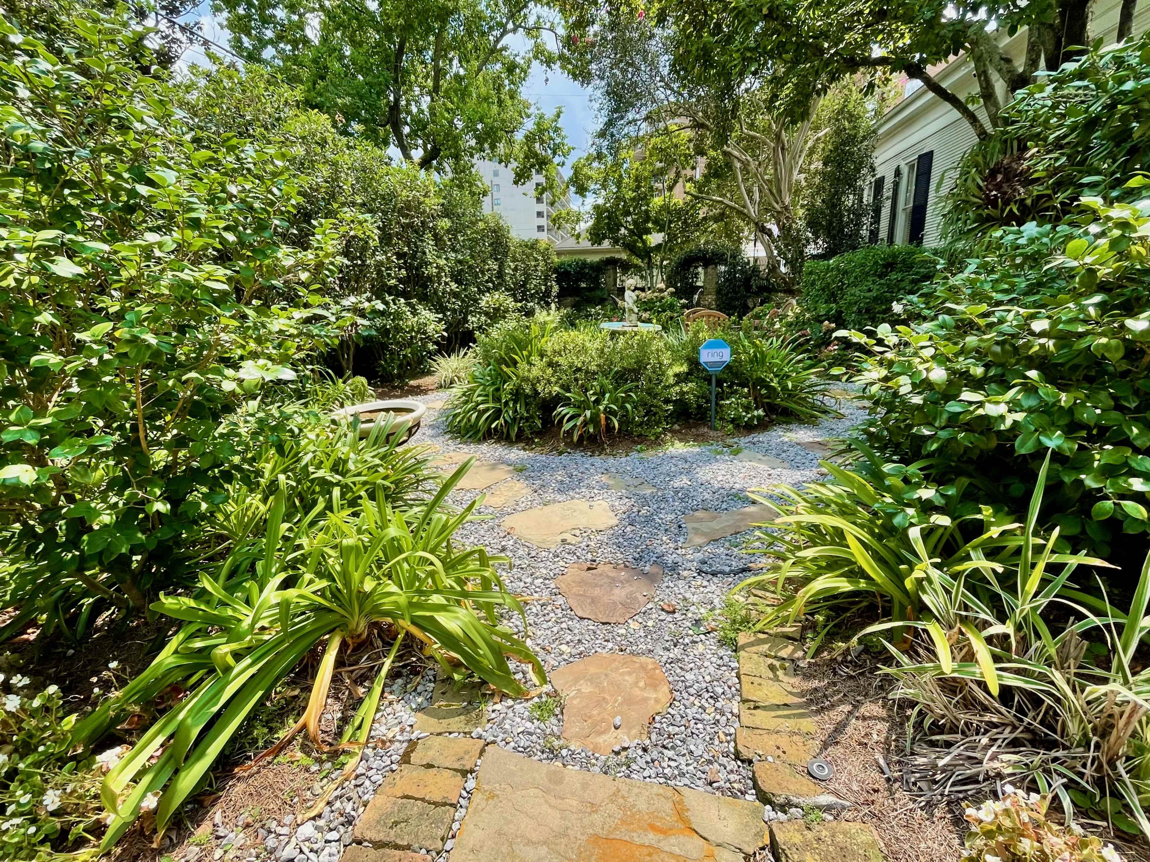 A stone pathway winds through a lush garden filled with greenery and shrubs.