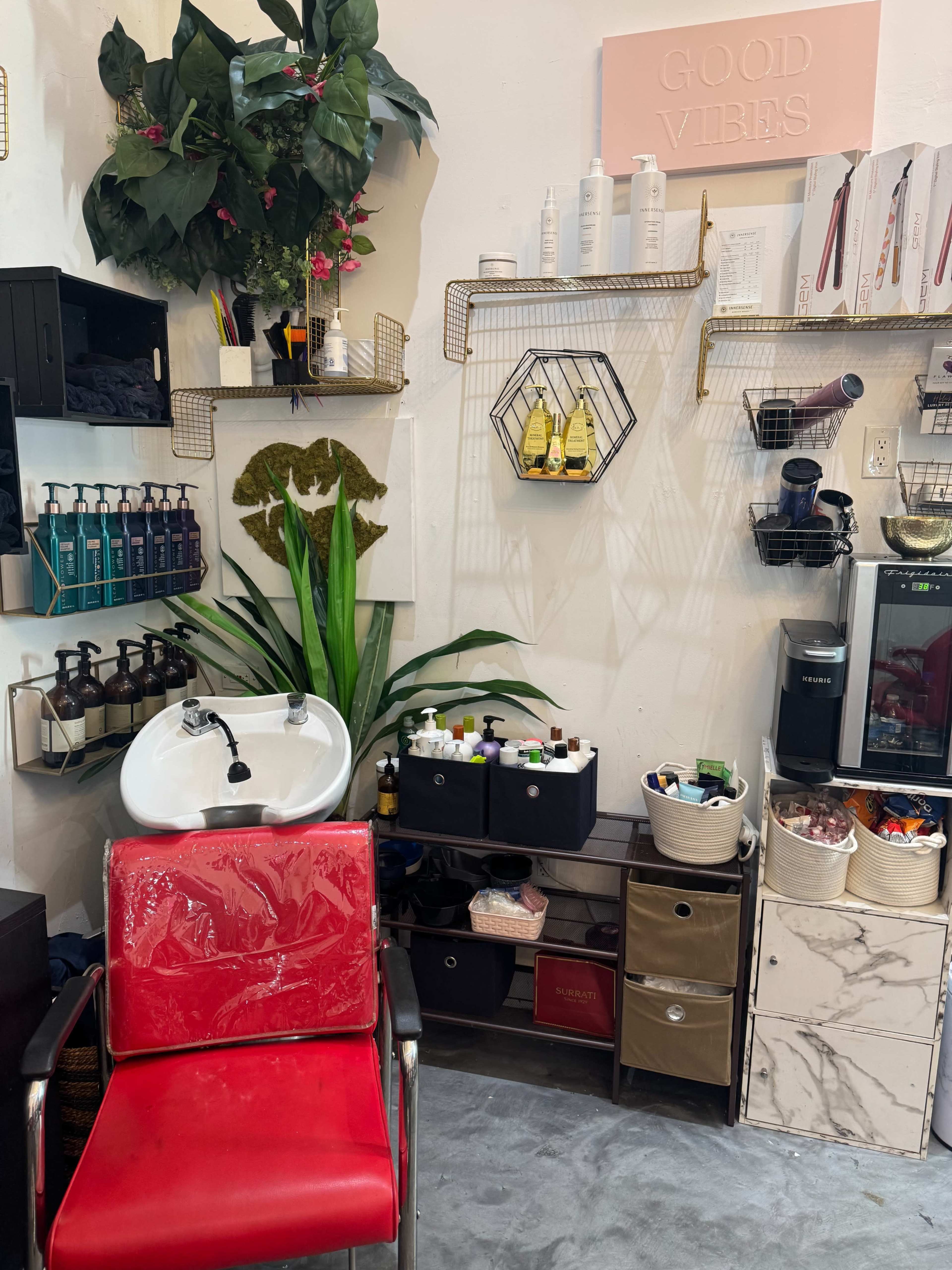 The image shows a hair salon interior featuring a red salon chair, a washing sink, and shelves with various hair care products and accessories.