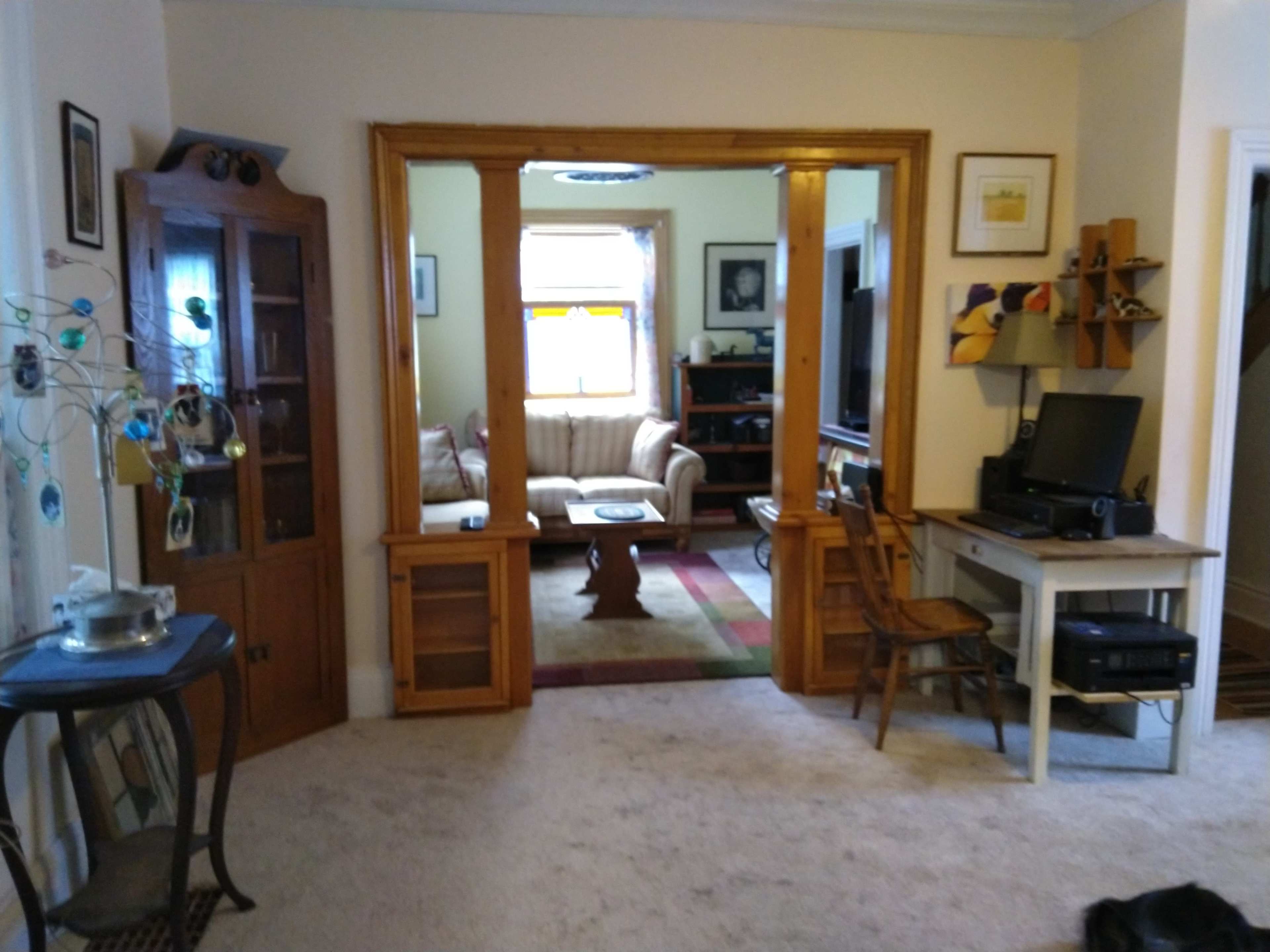 A living room area viewed from an adjoining room, featuring a wooden divider, a sofa, a television, and various decorative items.