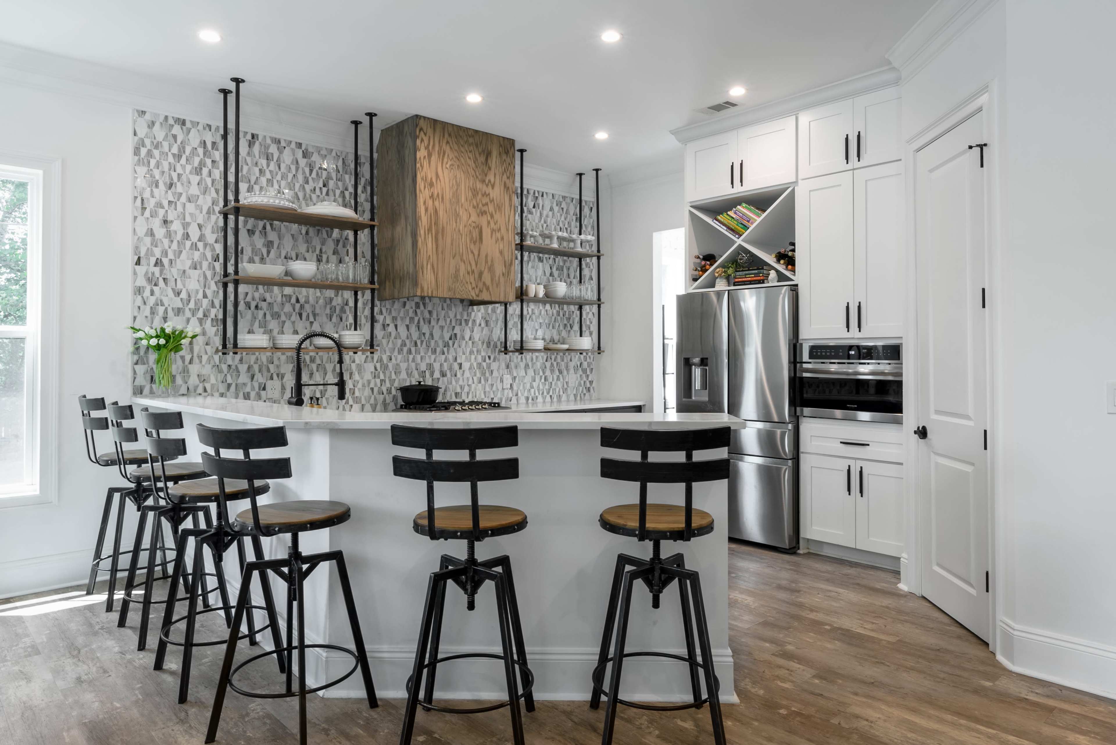 A modern kitchen features a central island with bar stools, sleek cabinetry, and tiled backsplash.
