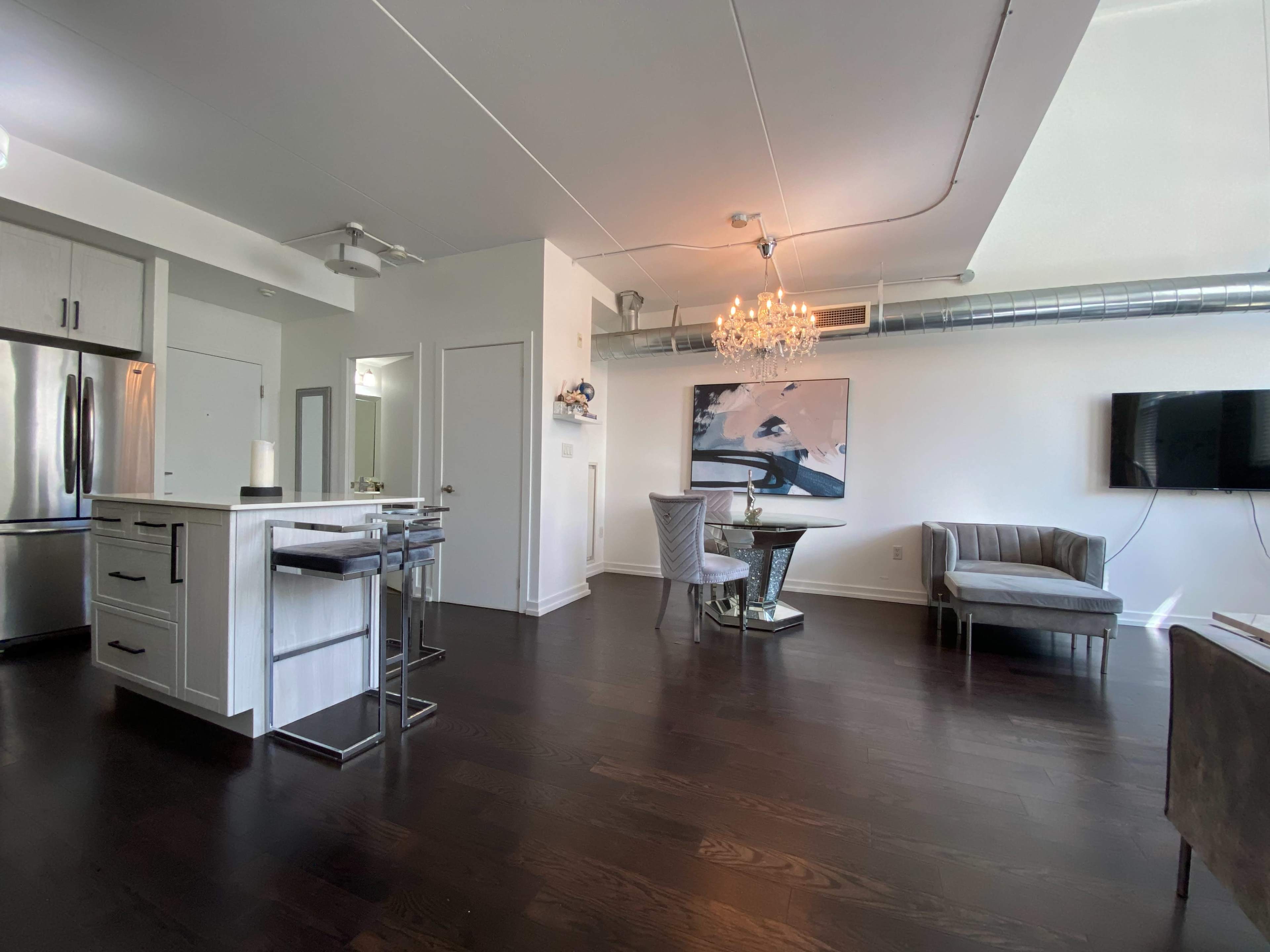 A modern living space with a kitchen area, dining table, and a sitting area, featuring hardwood floors and contemporary furnishings.