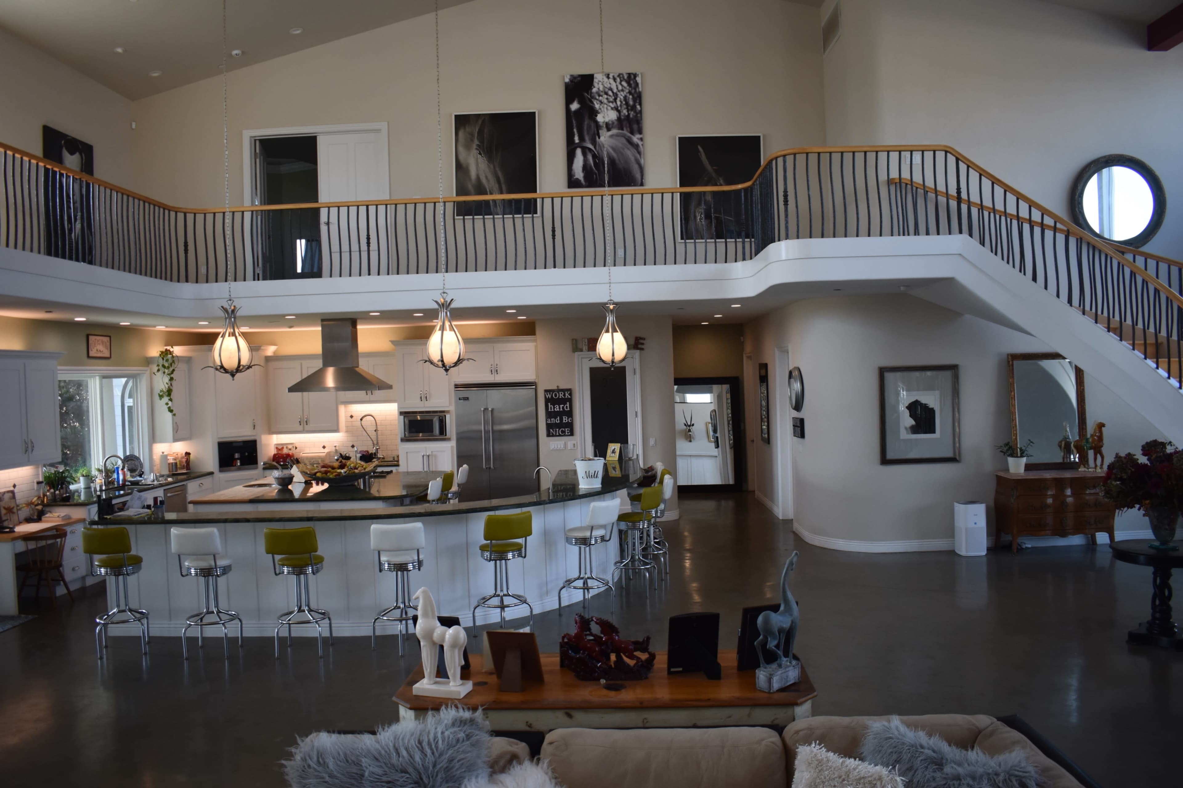 The image shows a spacious, modern living area with a kitchen island, seating area, and a balcony overlooking the space.
