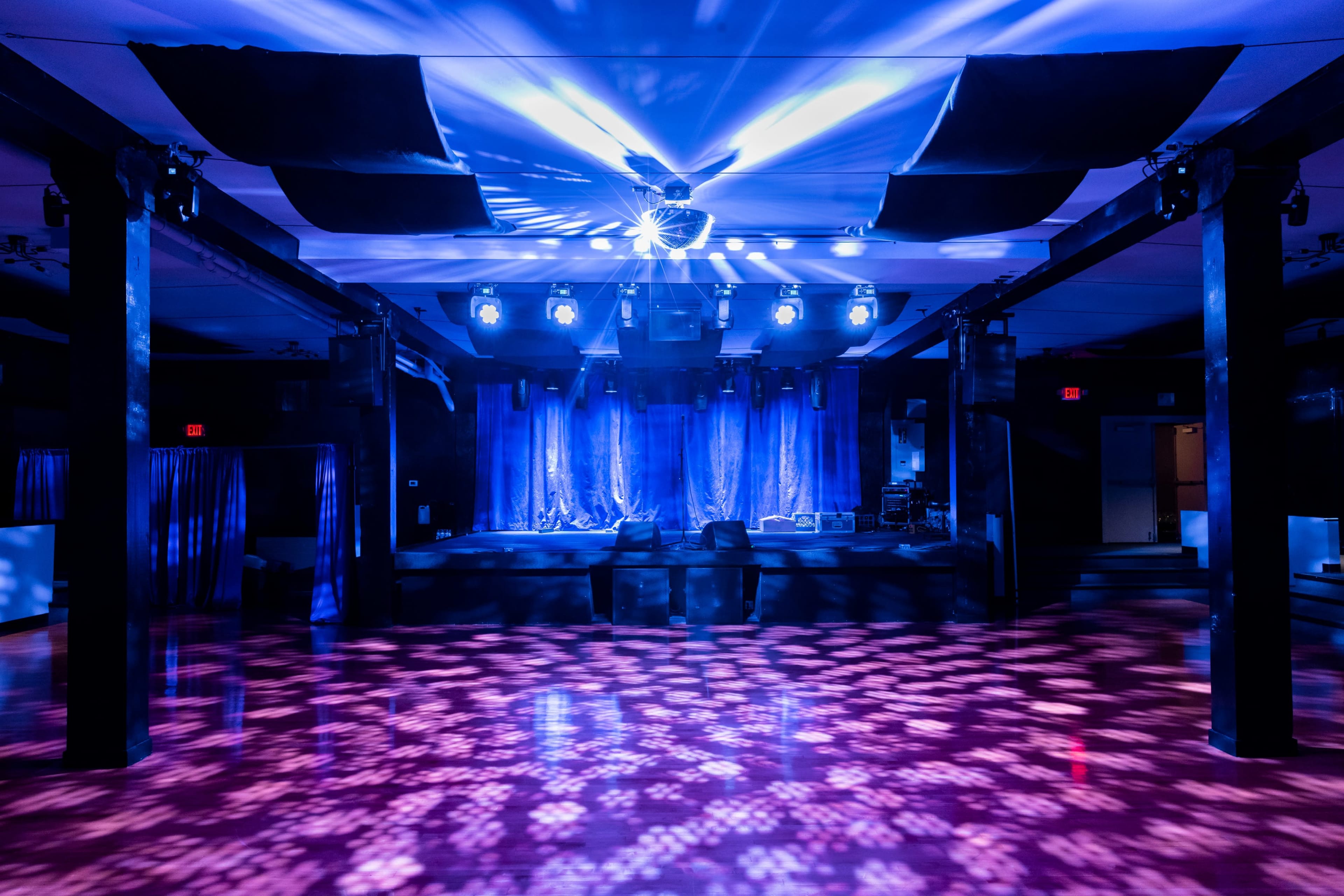 The image shows an empty dance floor illuminated by colorful spotlights and a disco ball in a dimly lit venue.