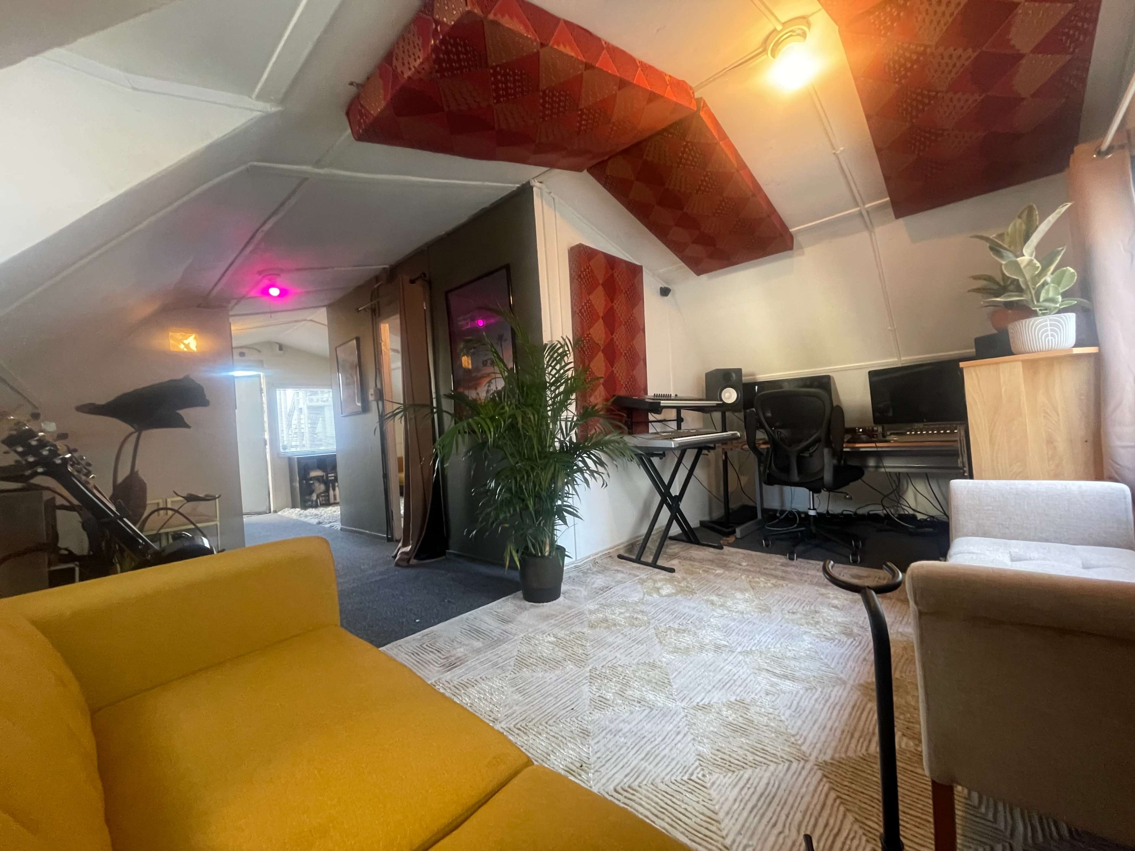 A cozy room with a yellow sofa, musical equipment, and a plant, featuring colorful patterned ceilings and a doorway leading to another space.