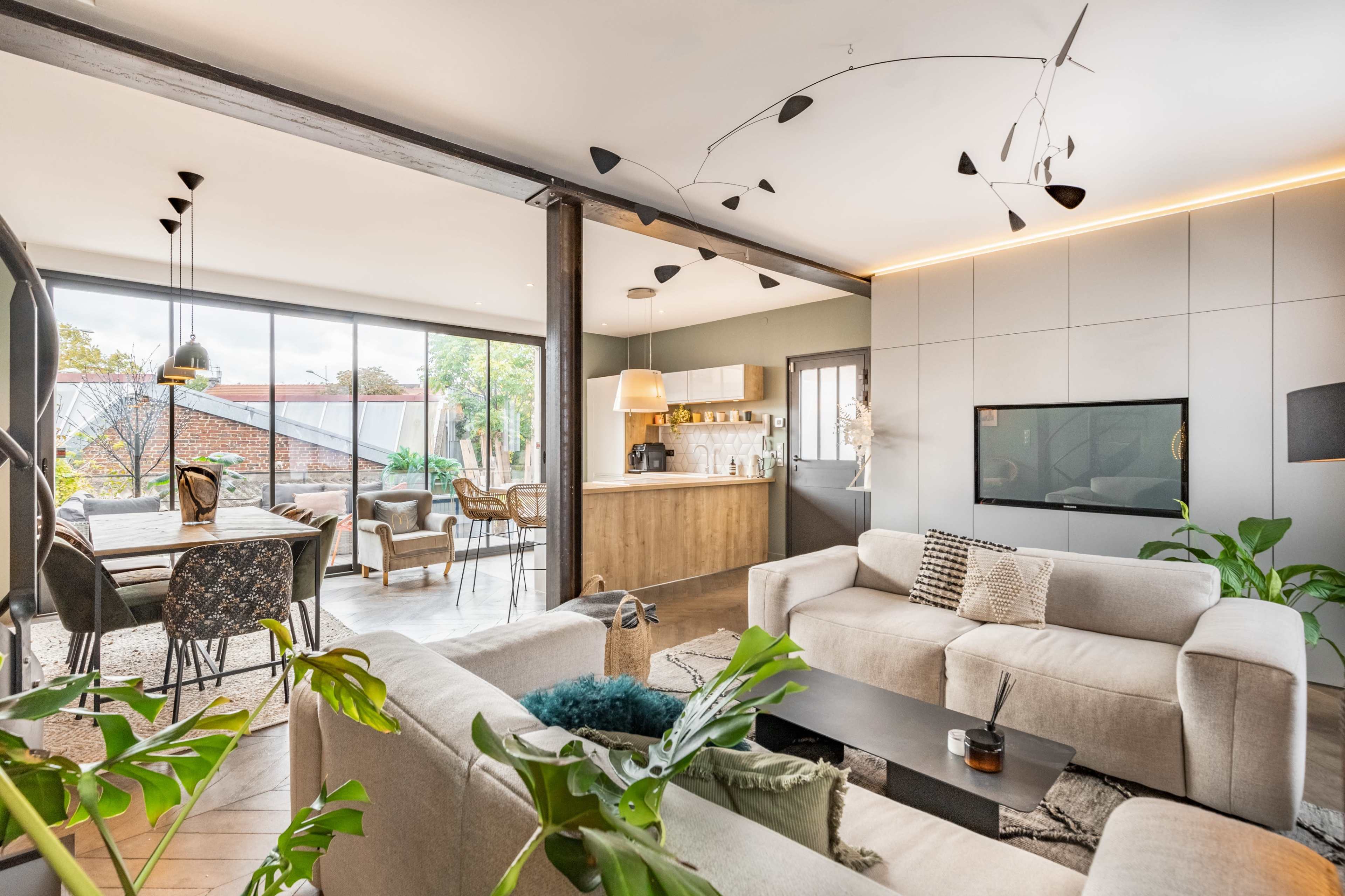 A modern living space featuring a light-colored sofa, a black coffee table, and a kitchen area visible in the background through large windows.