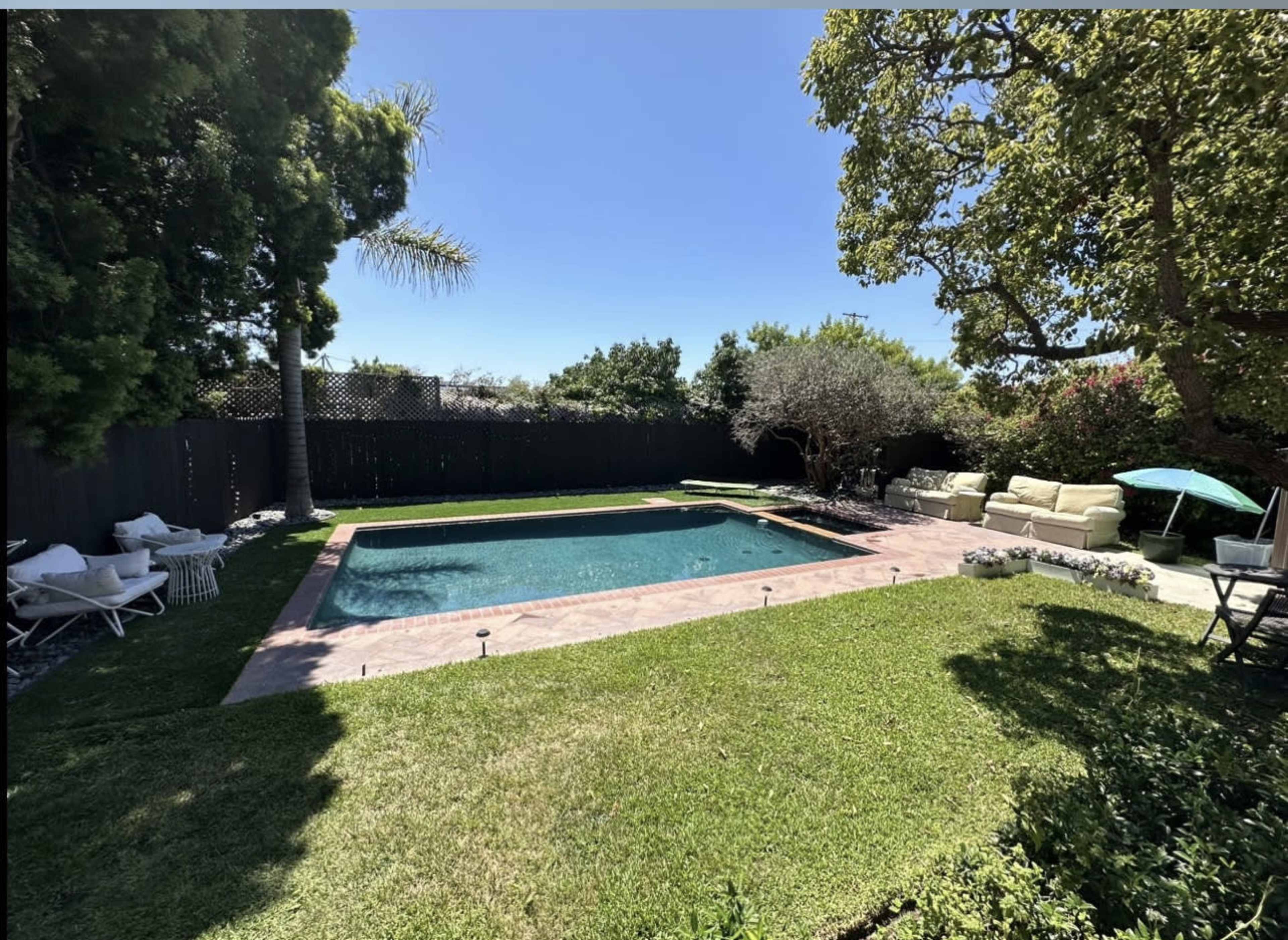 A rectangular swimming pool is surrounded by grass and trees in a well-maintained backyard.