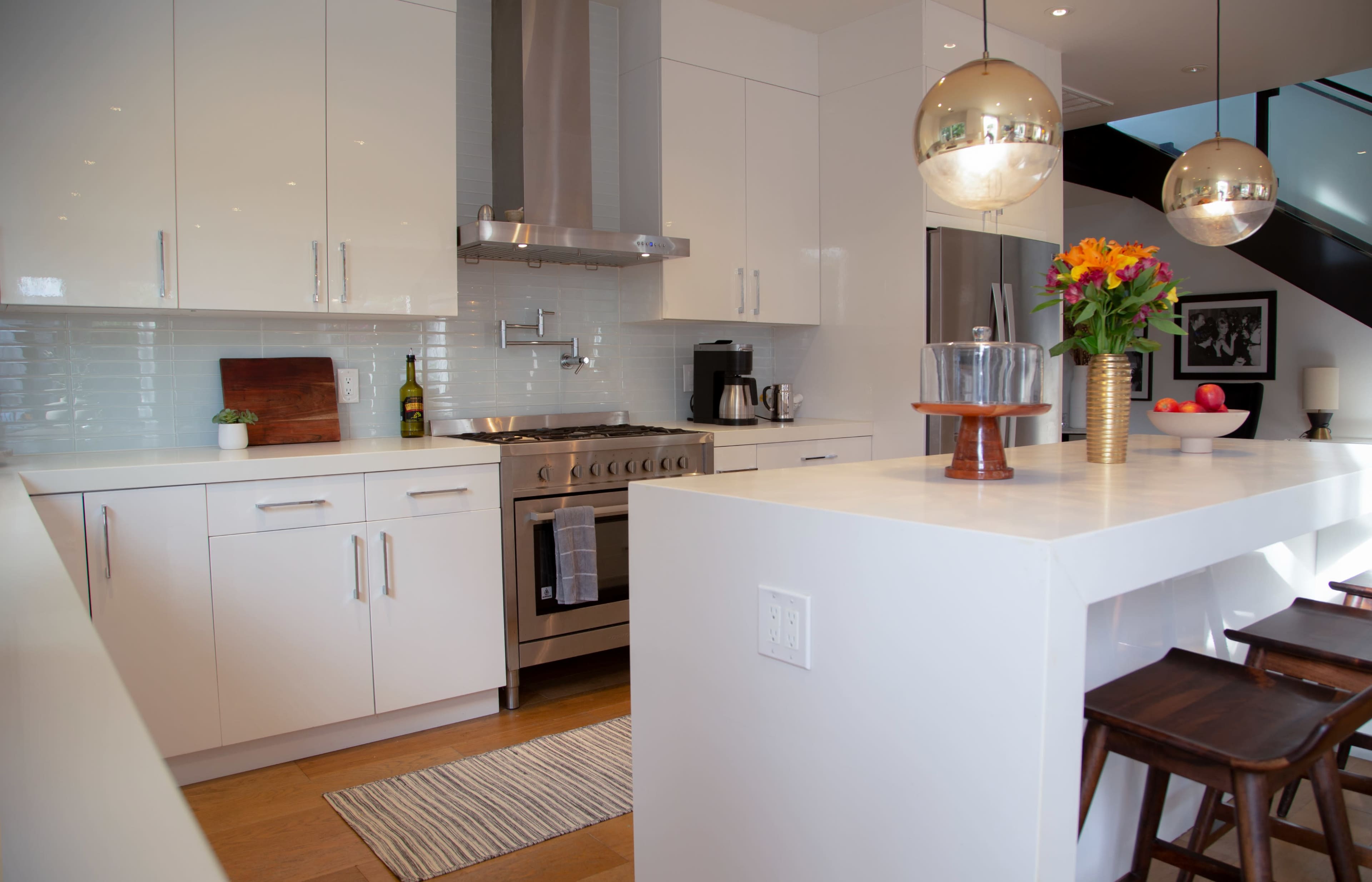 A modern kitchen features white cabinetry, stainless steel appliances, and a central island with bar stools and a bouquet of flowers.