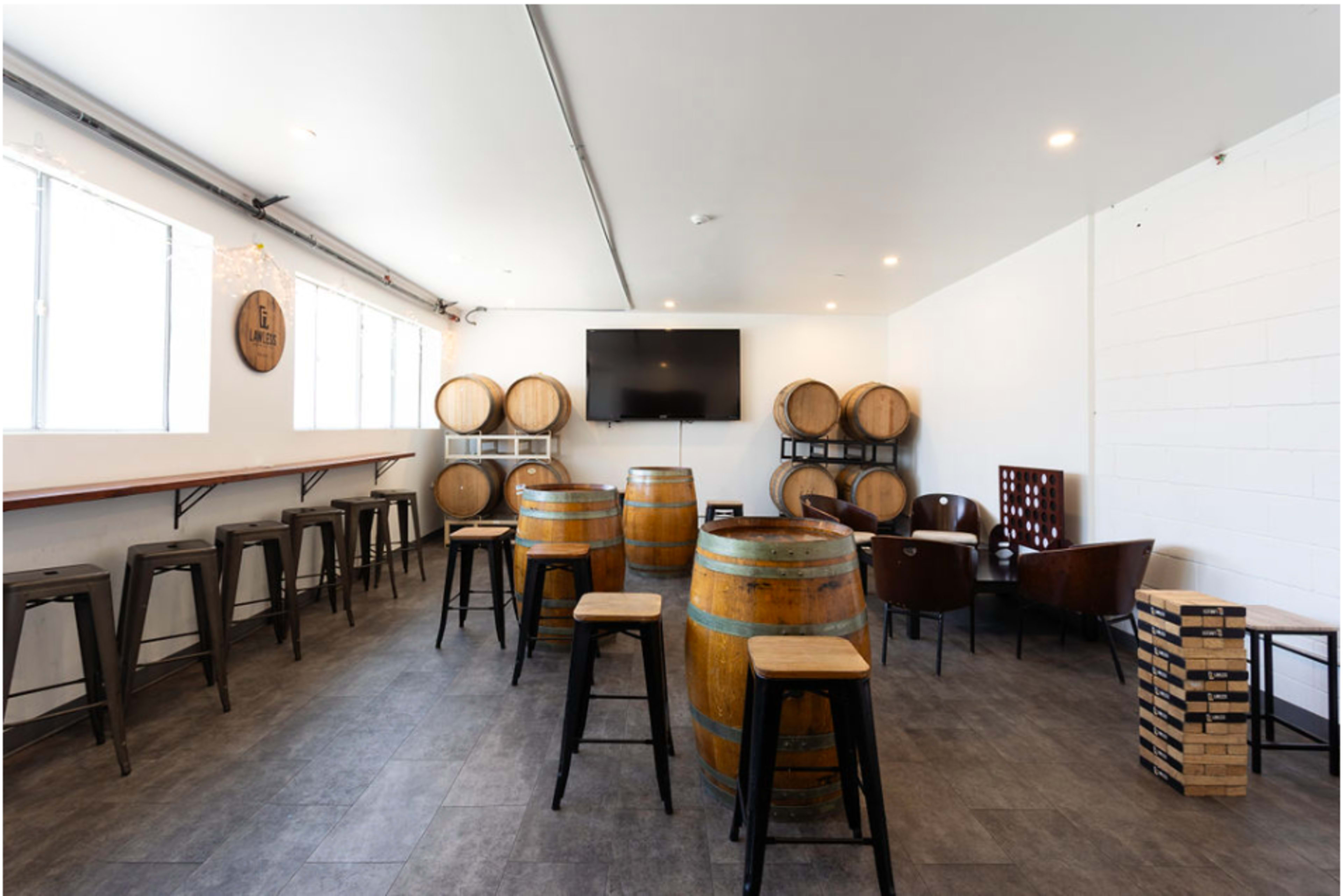 A spacious room with wooden barrels, seating tables, and chairs arranged around a wall-mounted television.