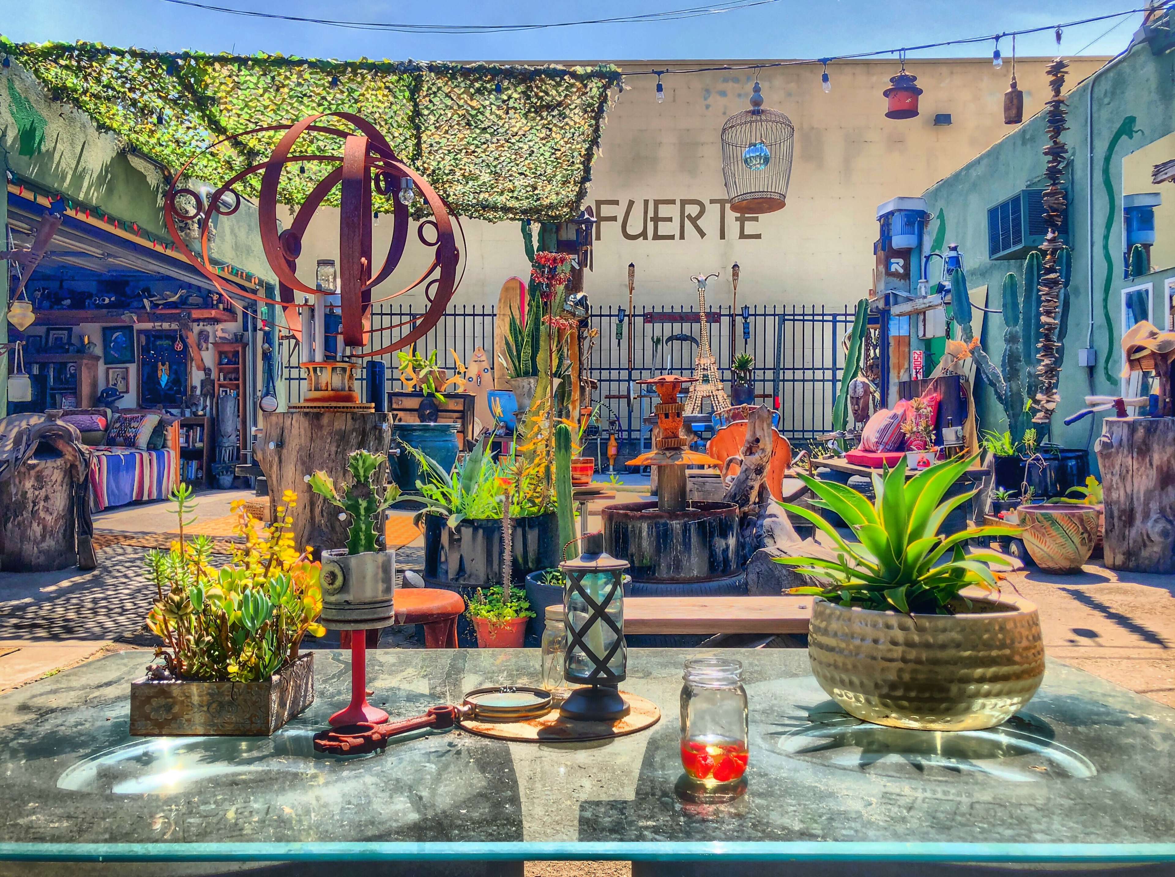 A vibrant outdoor space filled with eclectic decor, including plants, sculptures, and furniture arranged around a central table.