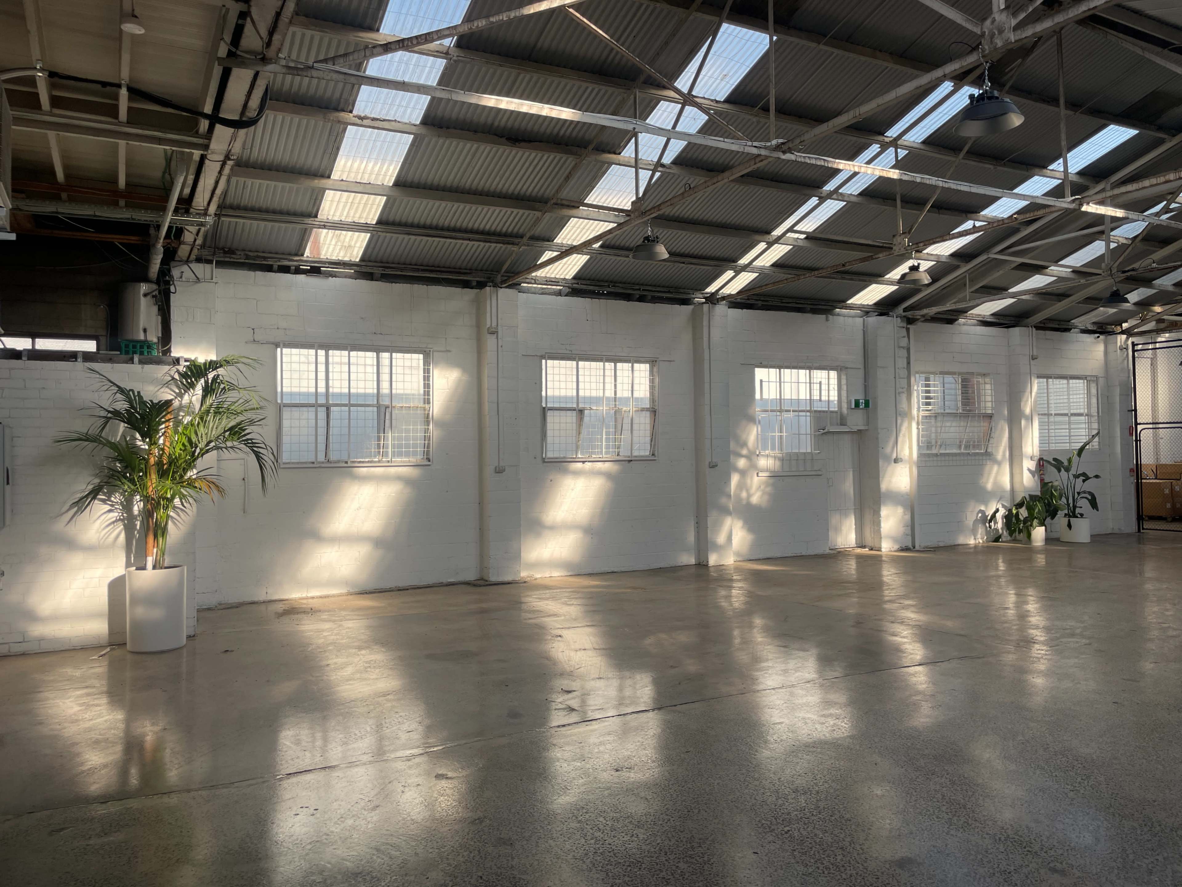 The image shows a spacious industrial interior with white walls, large windows, and sunlight casting shadows on the polished concrete floor.