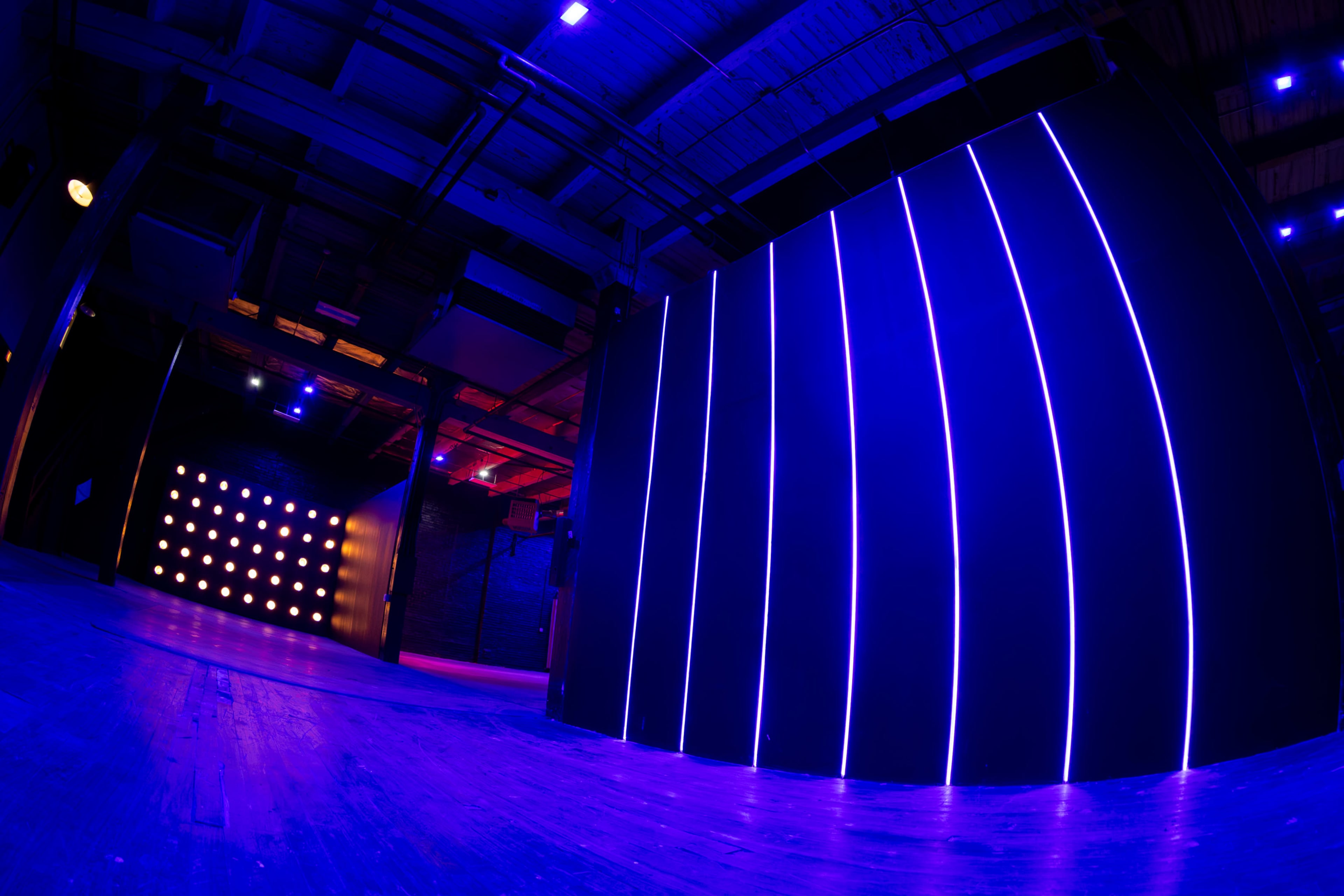 The image shows a dimly lit room with contrasting walls featuring vertical neon lights and a panel of illuminated dots.
