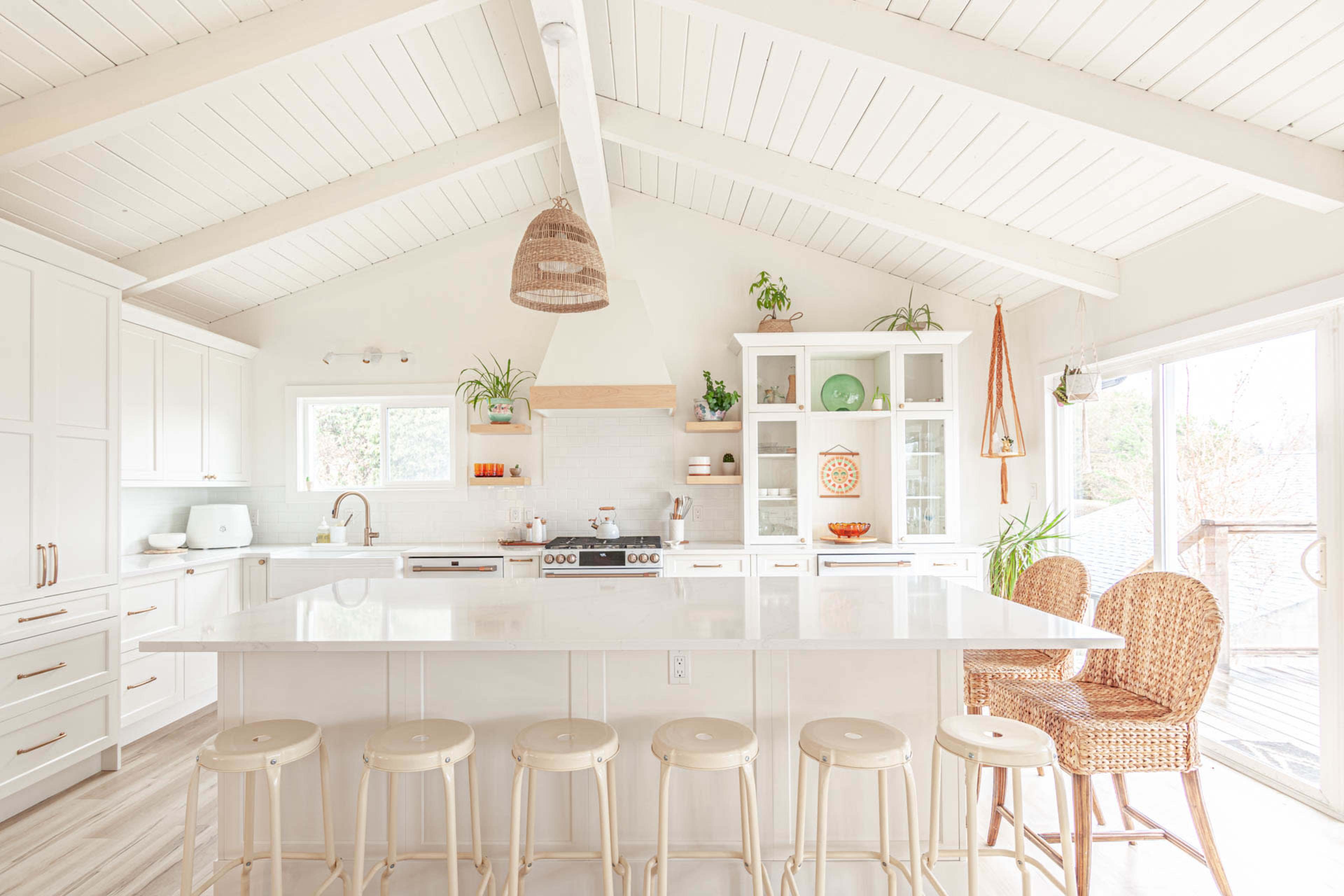 A bright, modern kitchen features a large island with seating, white cabinetry, and natural light streaming through windows.