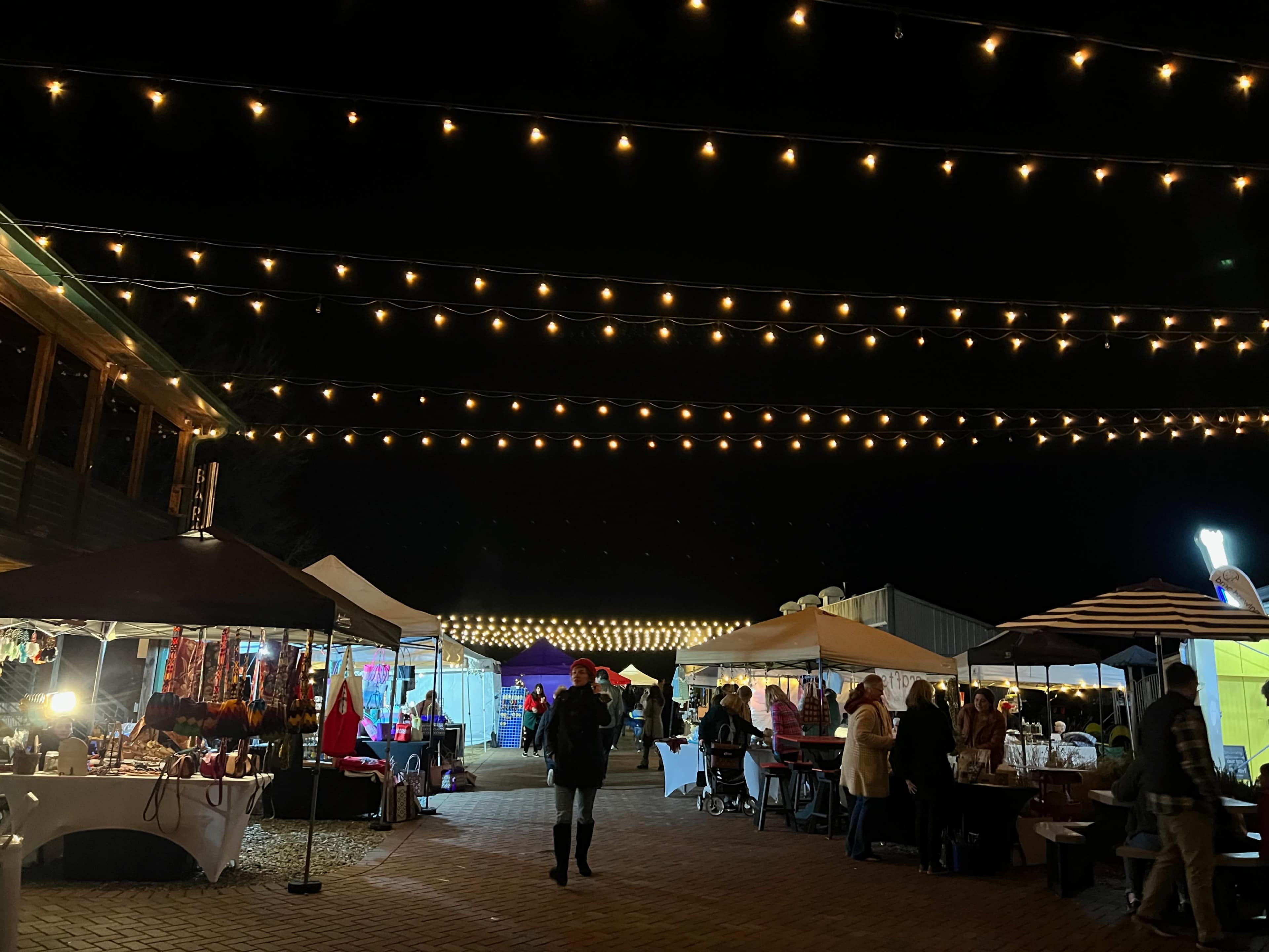 A night market scene features stalls with various goods, connected by overhead string lights, as people shop and socialize.