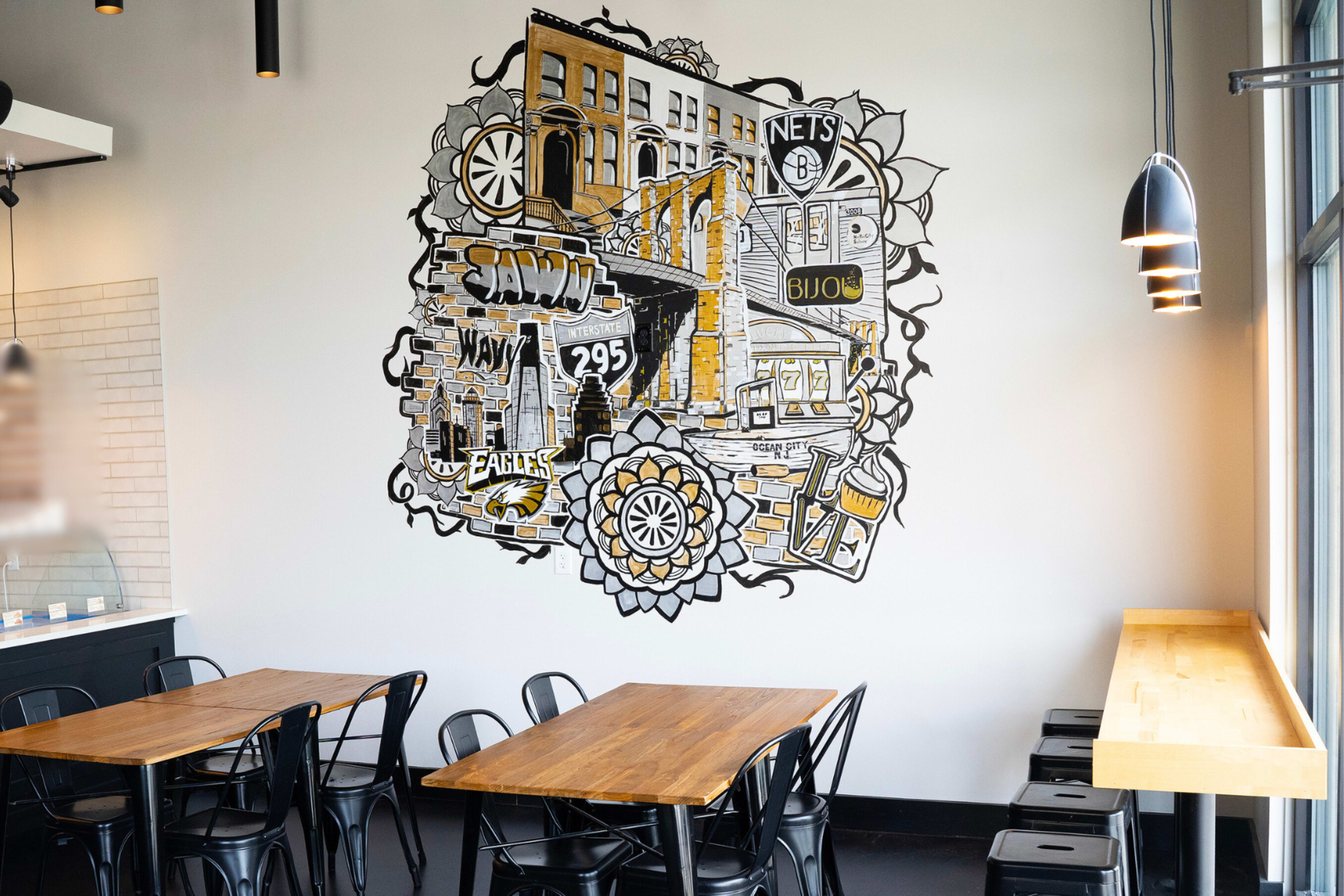 A large mural depicting a cityscape is painted on the wall of a dining area, surrounded by wooden tables and black chairs.