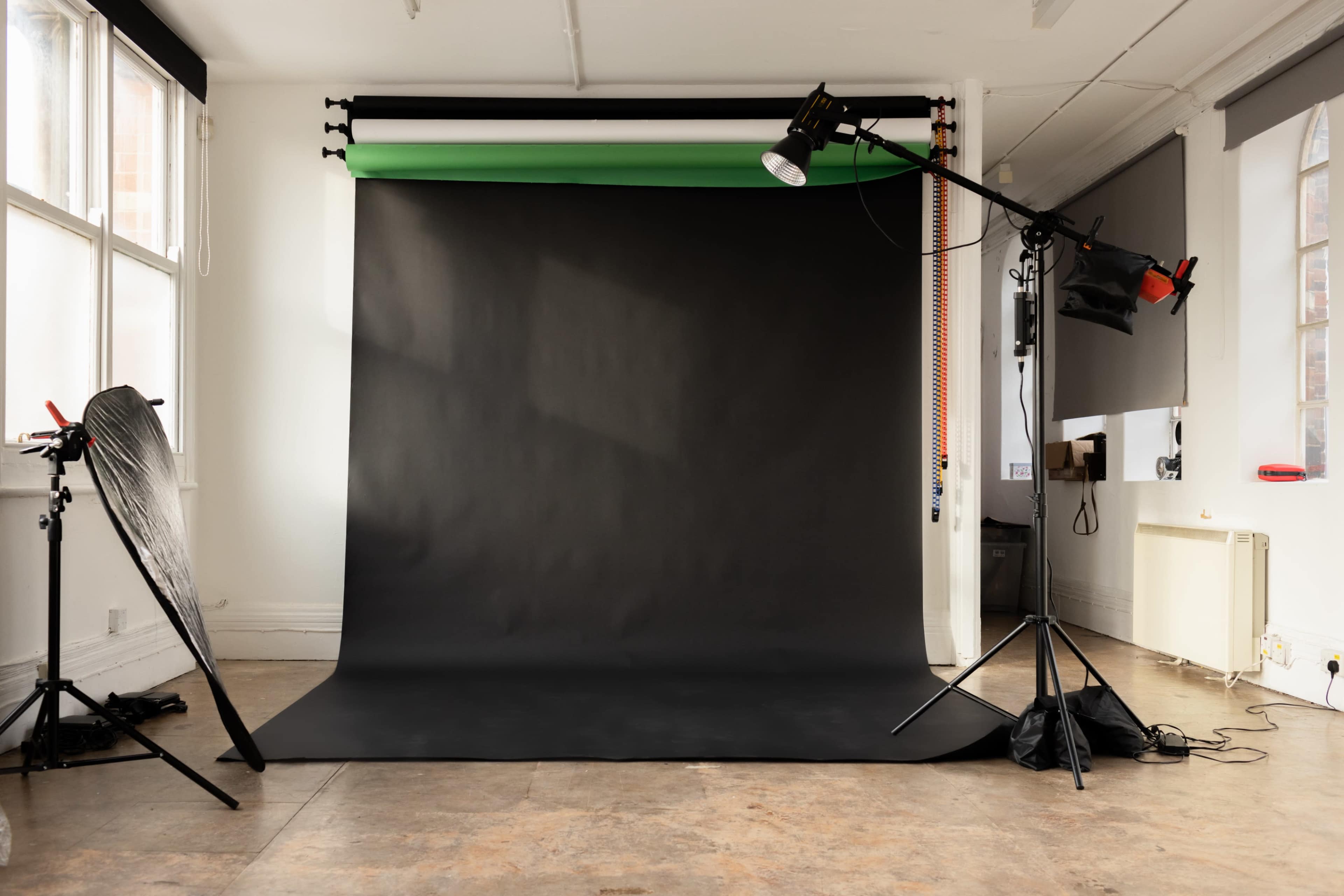 A photography studio featuring a black backdrop, various lighting equipment, and a spacious, minimalistic interior.