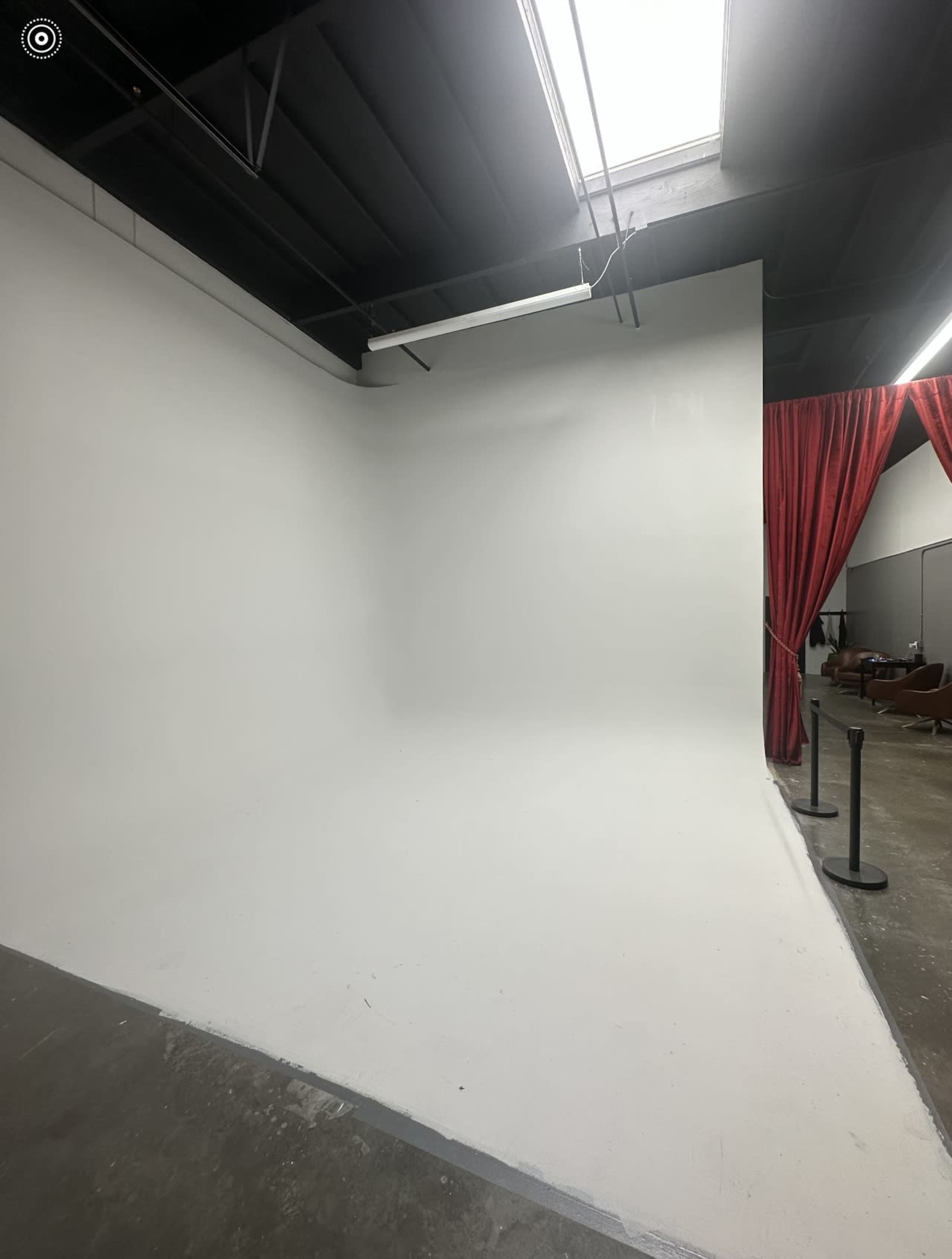 A spacious studio with a blank white backdrop and red curtains on one side.