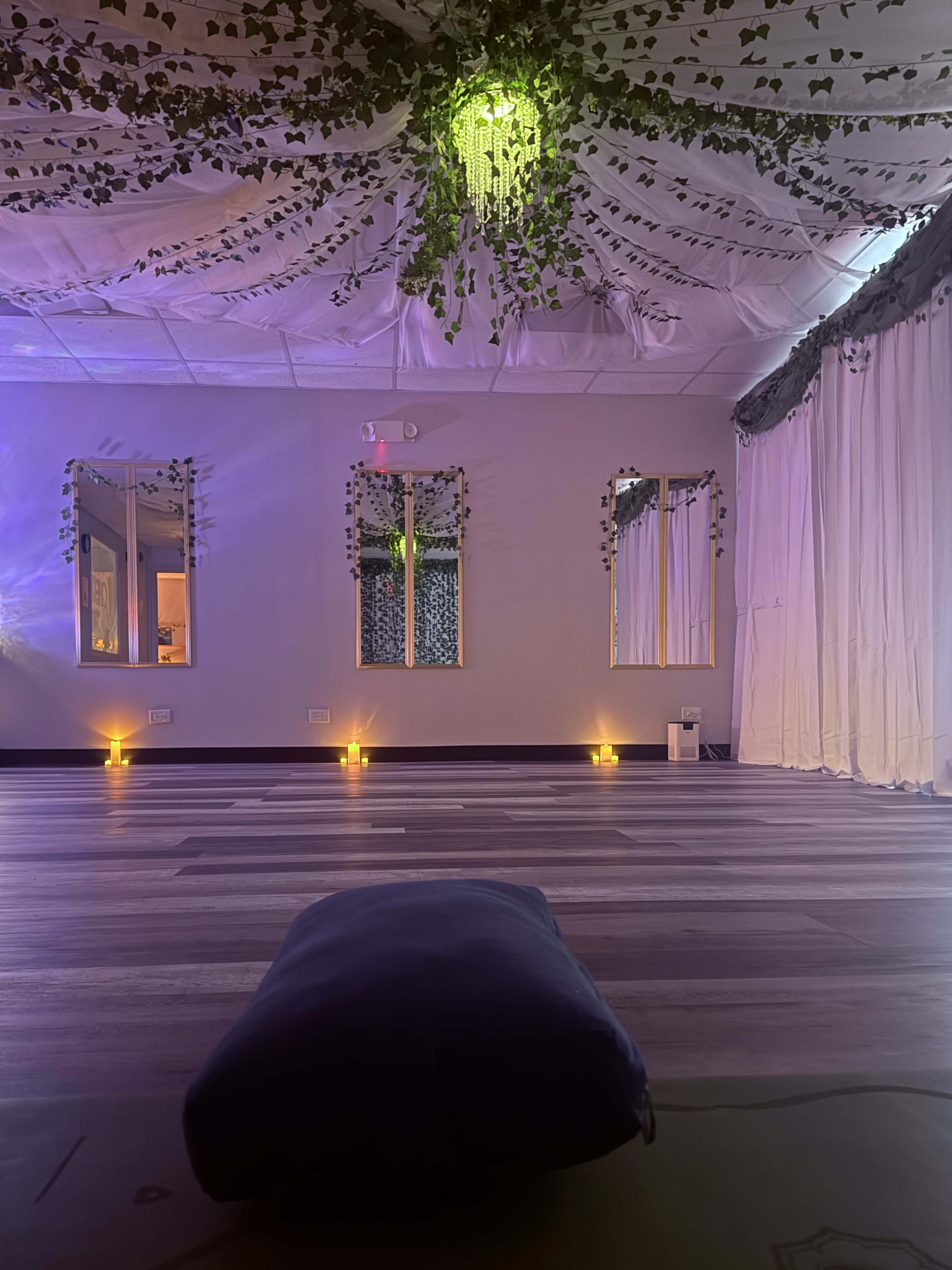 The image shows a tranquil yoga studio with a decorated ceiling, mirrors on the walls, and dim lighting from candles.