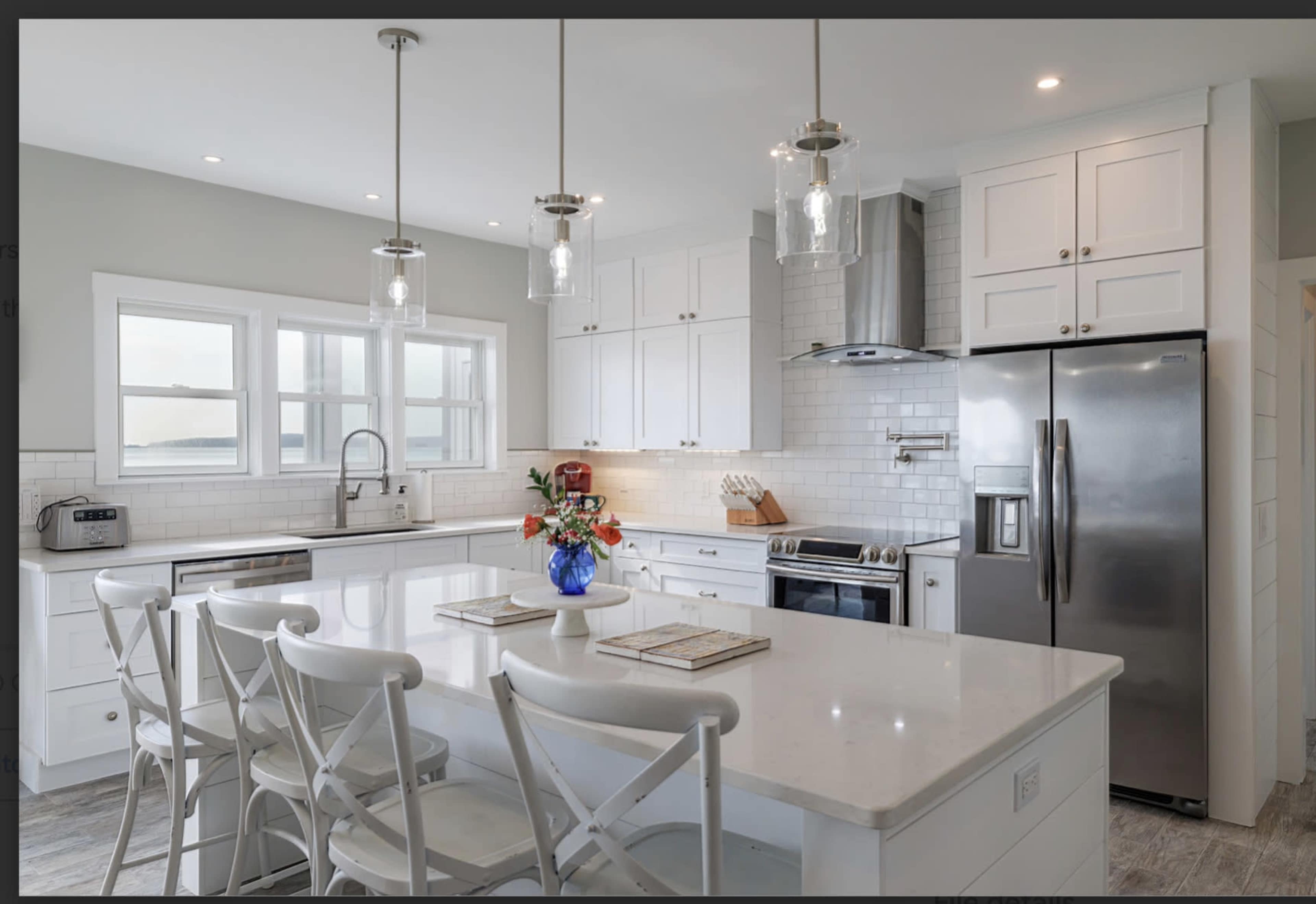 A modern kitchen features white cabinetry, a large island with seating, stainless steel appliances, and pendant lighting.